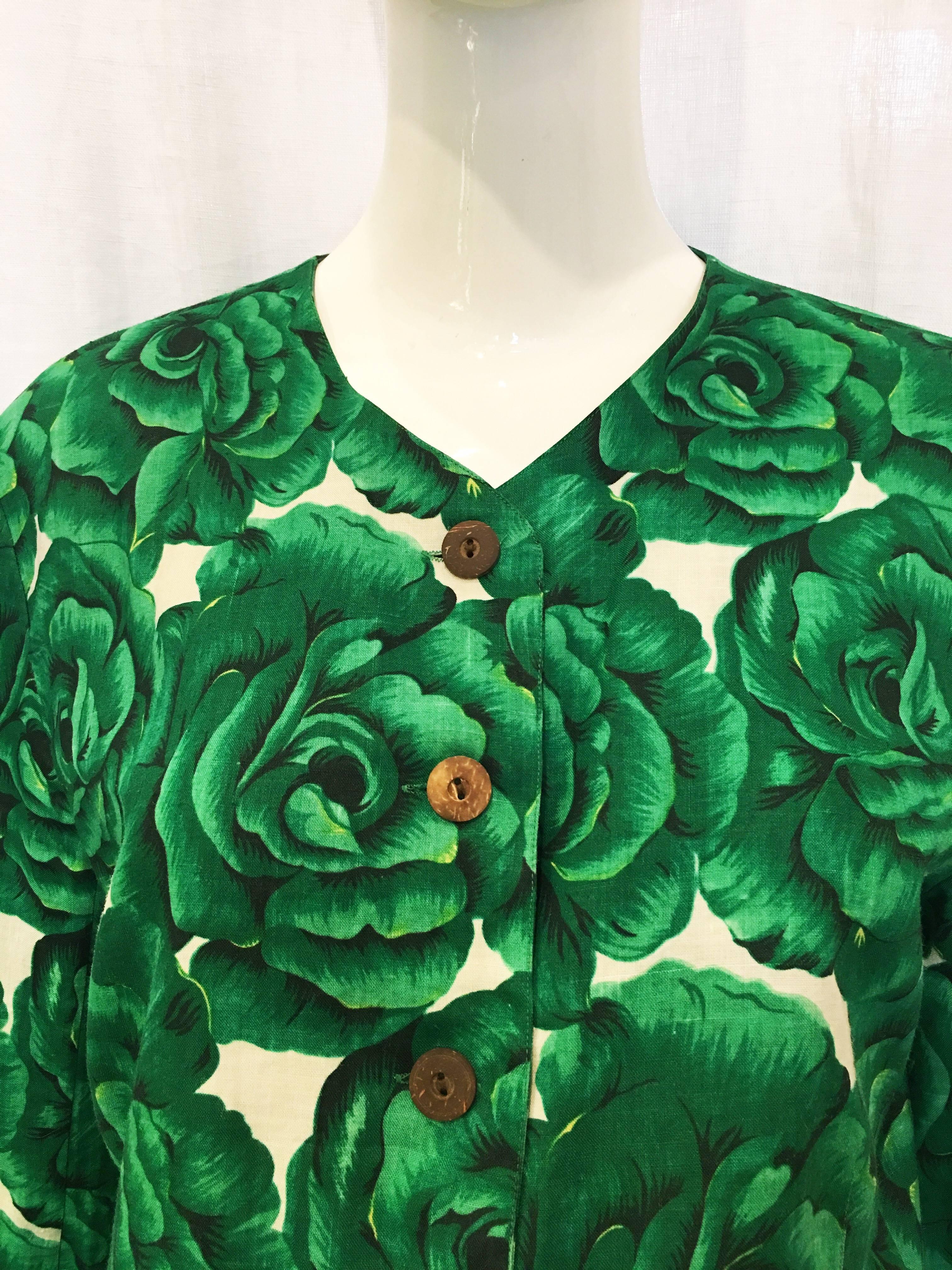 Lightweight white collarless jacket with all-over green rose print. Six wooden buttons down the front as well as two front pockets. Three decorative wooden buttons at cuffs of sleeves. A bright accompaniment to a springtime work ensemble or as a