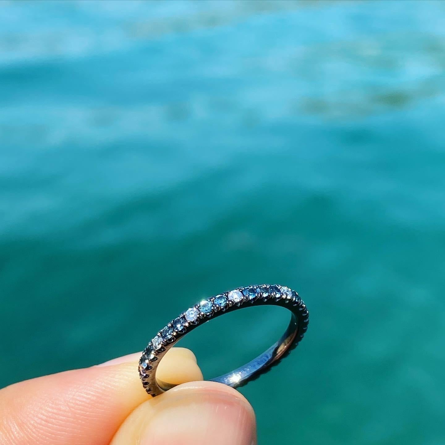 Evoking the blue tones of the Aegean Sea, this mixed eternity band features varying tones of blue topaz, bluish grey sapphire, blue (teal) diamonds, grey diamonds & white diamonds. 

Total carat weight: 0.6 (for size 6)
Total width: 1.8mm (1.5mm