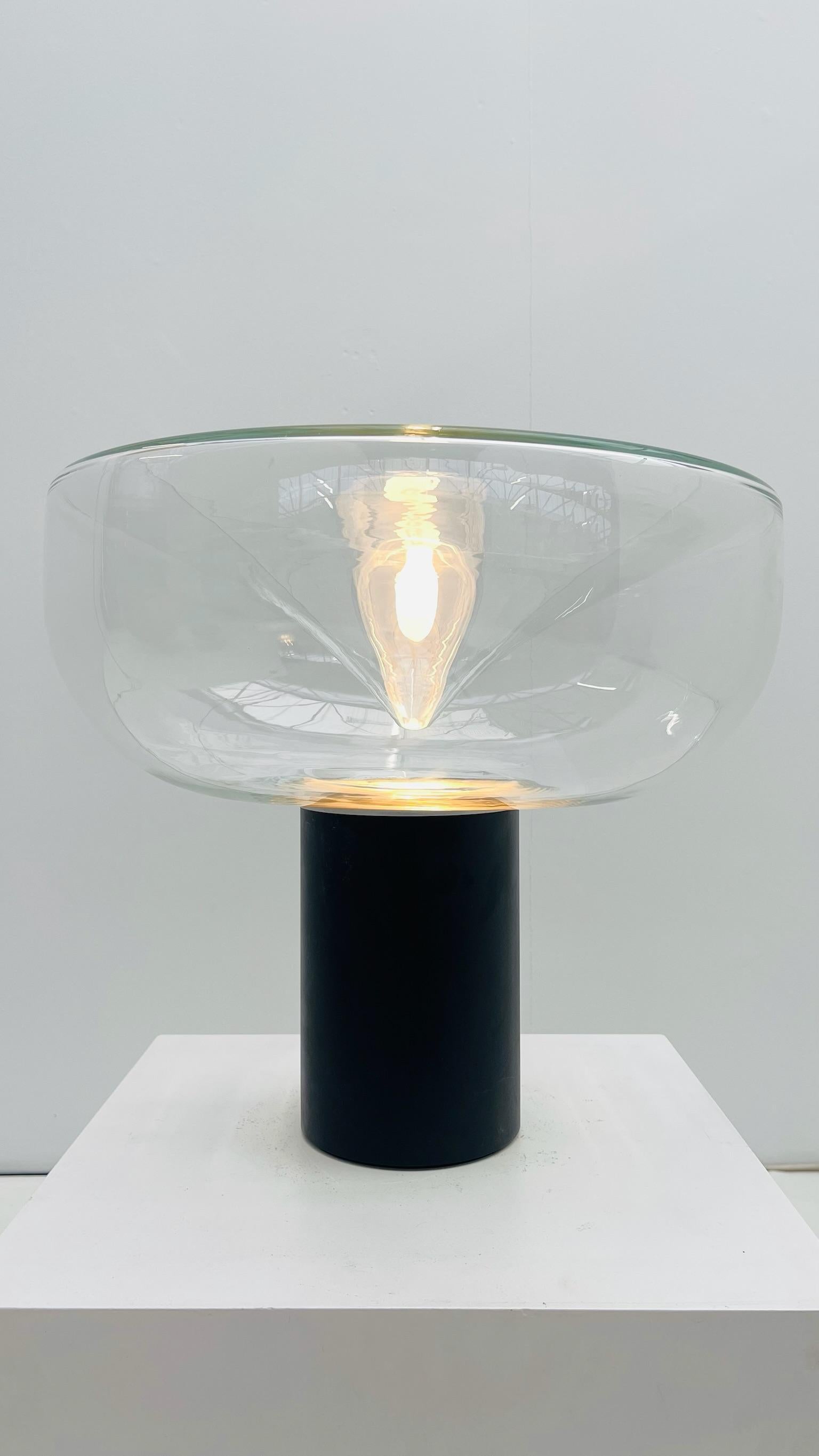 La lámpara de mesa Aella 50 tiene una base de aluminio pintado y una pantalla de vidrio soplado en su versión grande. Su nombre, que significa 