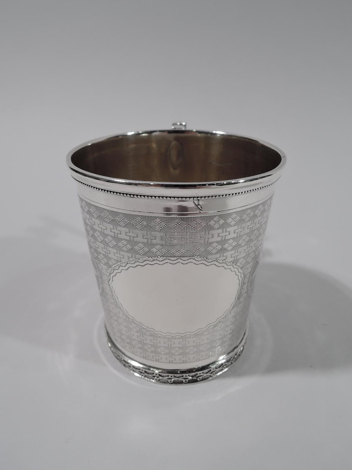 Aesthetic classical coin silver baby cup. Straight sides with bracket handle. Oval frames with wavy borders of which one vacant and two inset with paterae. Engine-turned geometric-patterned ground. A stunner. Marked “Coin / 2” with maker’s stamp for