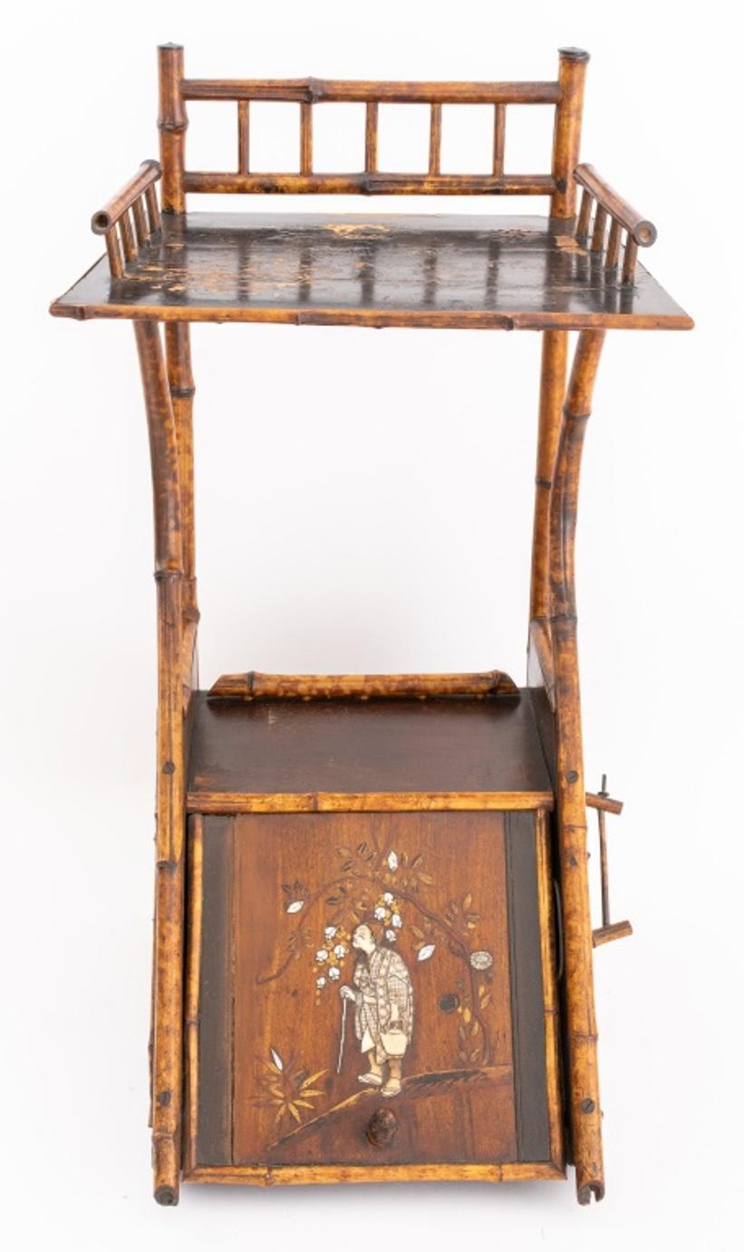 Japonaisme bamboo and faux lacquer tiered coal scuttle with paper rack above angled scuttle door with parquetry, bone and mother-of-pearl inlaid Japanese figure opening to reveal a lead-lined coal bin. 

Dimensions: 33