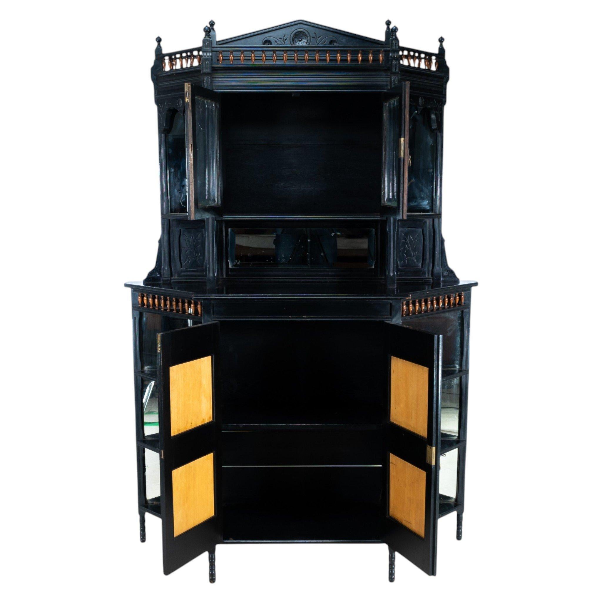 Attributed to William Watt, in the style of E. W. Godwin. An Aesthetic Movement ebonised walnut cabinet with carved floral decoration throughout. The upper section has an open display area with a turned gallery and fine finials, above a central