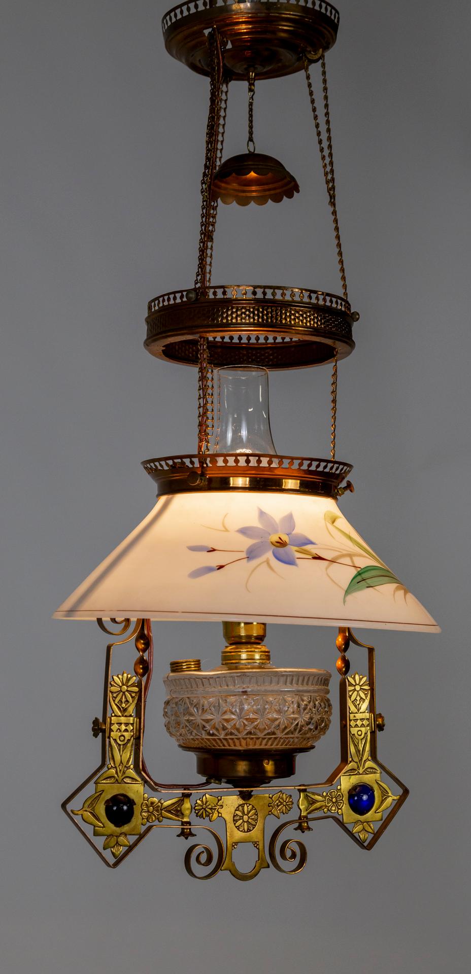 A lengthy, hanging, library oil lamp from the mid 1880s, in a striking Eastlake Victorian style; now electrified. A copper and brass, multitiered design on chains holding the shade, molded glass body, hurricane glass, and smoke cap. The milk glass