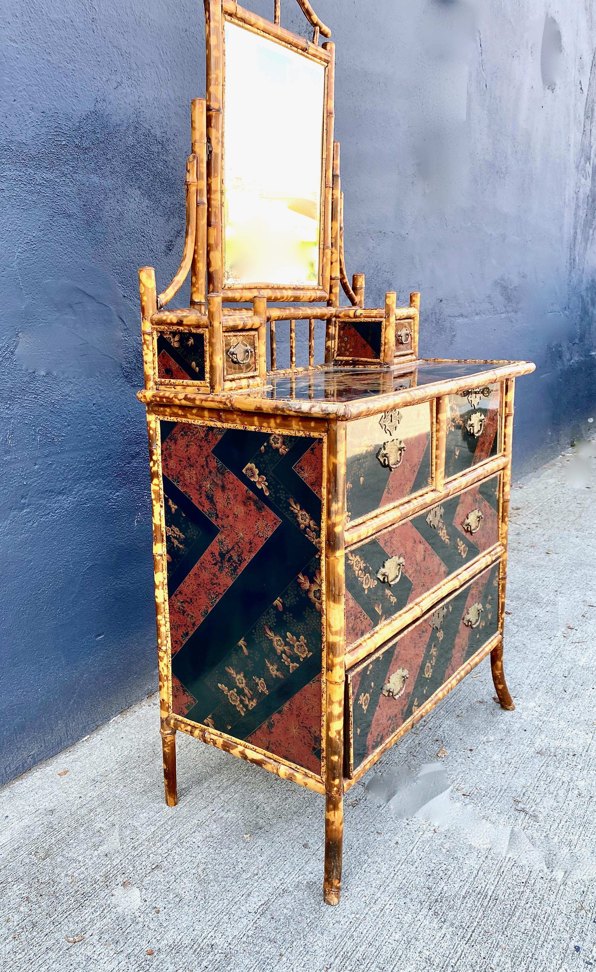 This is an exceptional example of an English Victorian Aesthetic Movement chest of drawers surmounted by its original mirror and a pair of small drawers on either side. The pine case has been beautifully detailed in burnt bamboo and encased in