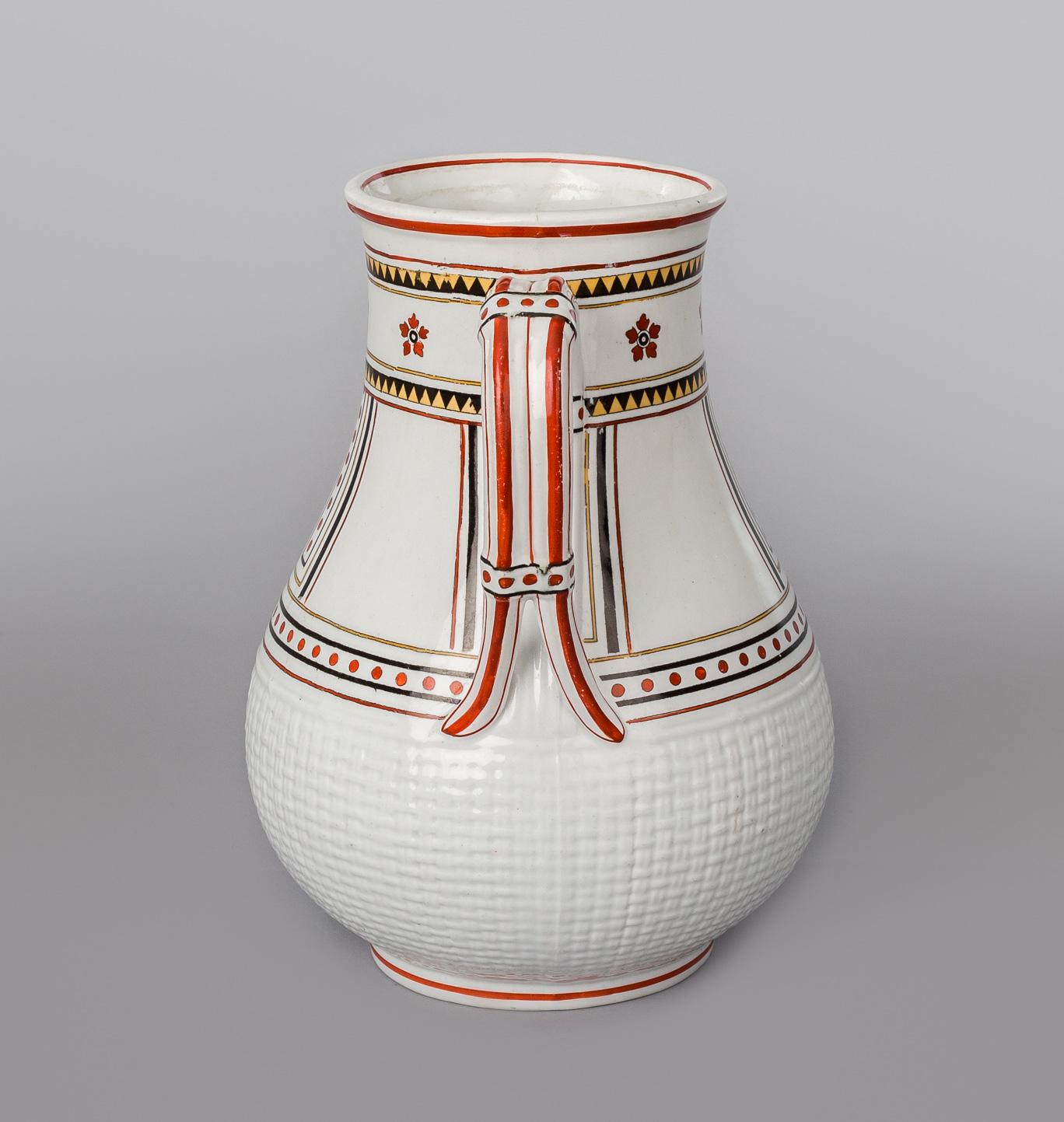 An Aesthetic Movement Minton pitcher or jug decorated with transferware geometric shapes in red, black and yellow on a white ground. It has a handle that splits at the bottom and there is no spout. The bottom is in a basket weave pattern. The