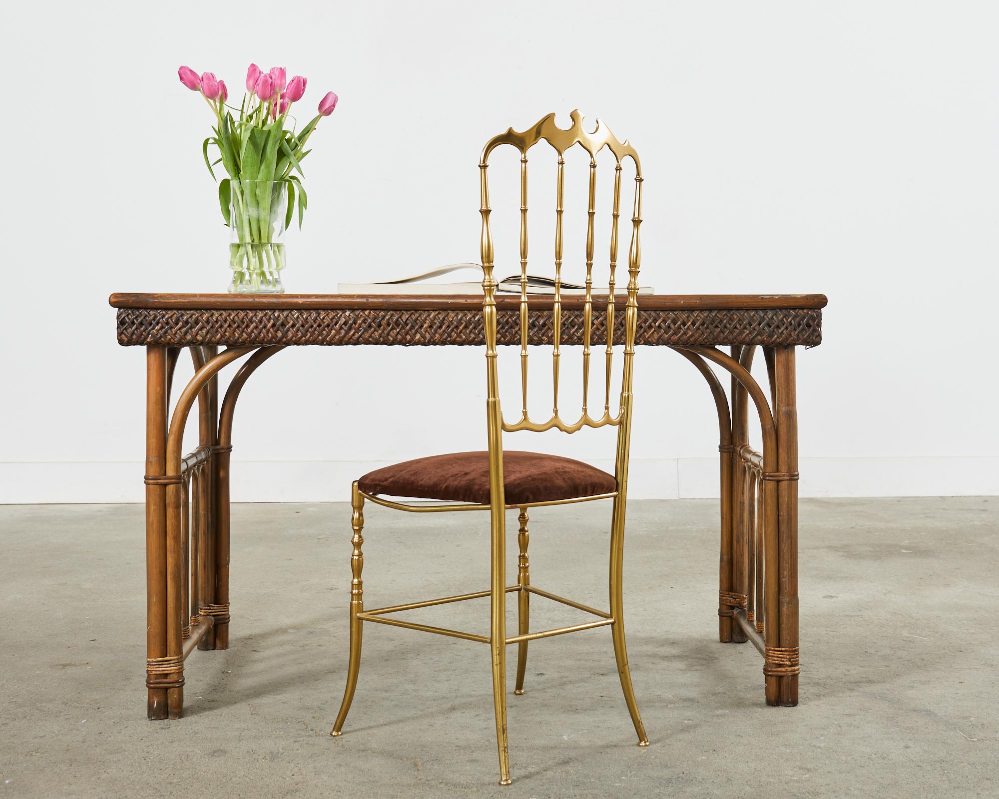 Gorgeous rattan and wicker library table or writing desk made in the English aesthetic movement style featuring a faux-slate top. The table is crafted from pole rattan with gracefully curved supports and decorative arches. The top has a formica