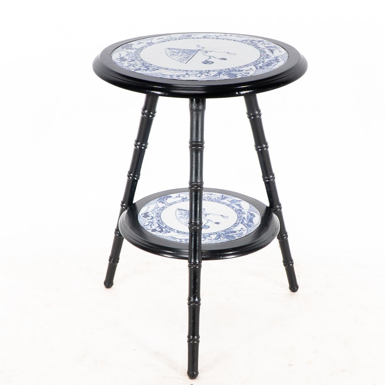 An Aesthetic Movement faux bamboo two tier ebonized side table, each tier inset with a Jeddo pattern plate made by Brown Westhead and Moore potteries featuring a Japanese fan with dancing butterflies and exotic birds and flowers to the border.