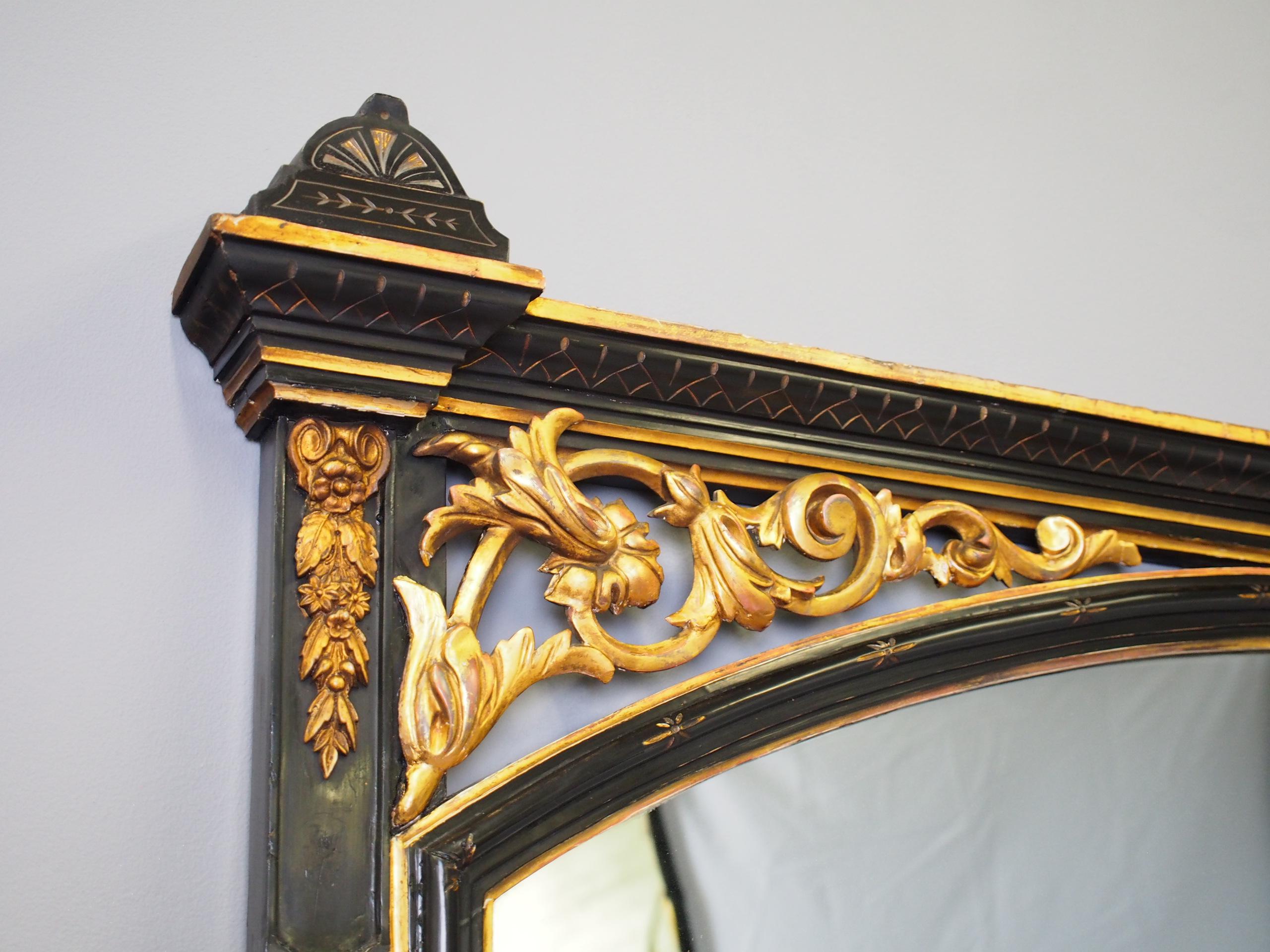 Aesthetic movement style gilded and ebonized wood overmantel mirror, circa 1880. The top has a mixture of painted and gilding, each end capped with 2 finials and beneath is an arched mirror with open fretwork and gilded foliate carving. There are 2