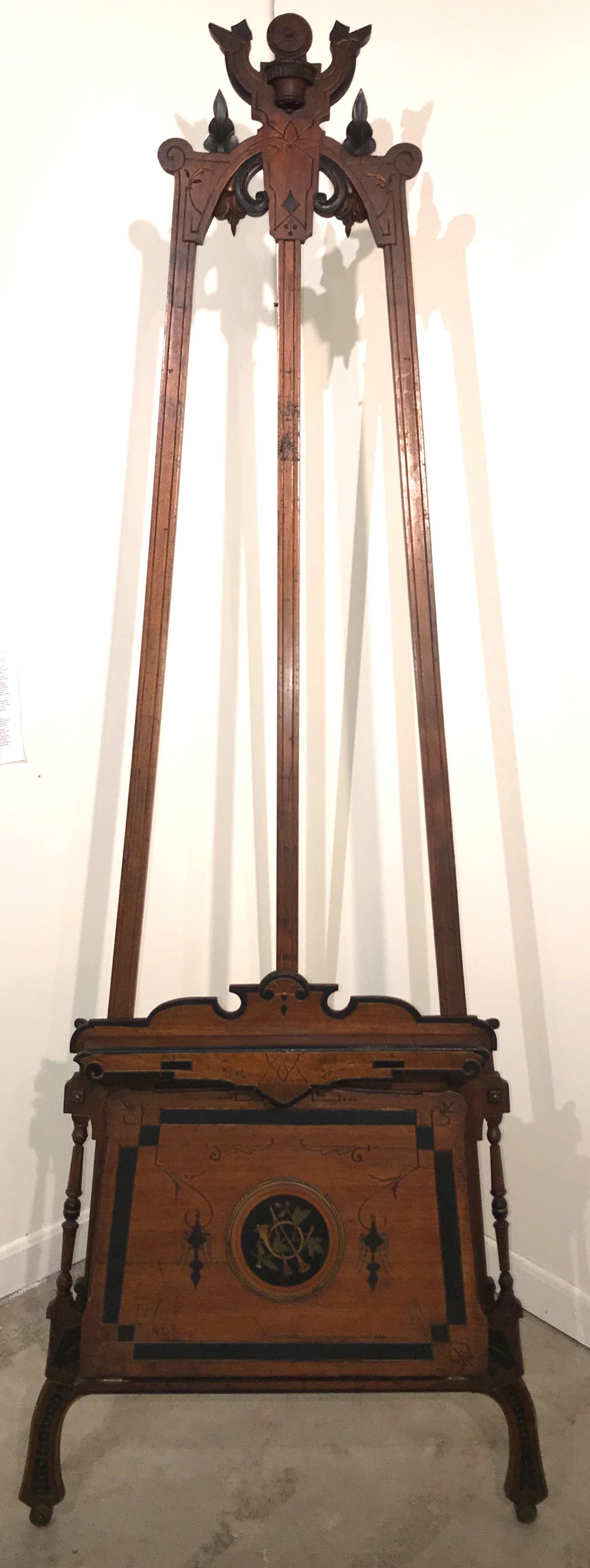 A beautiful example of a Victorian, late 19th century Aesthetic period walnut adjustable painting easel, with nicely carved fold-out portfolio at the base, decorated with satinwood inlaid musical instruments, scrollwork, turned outer support columns