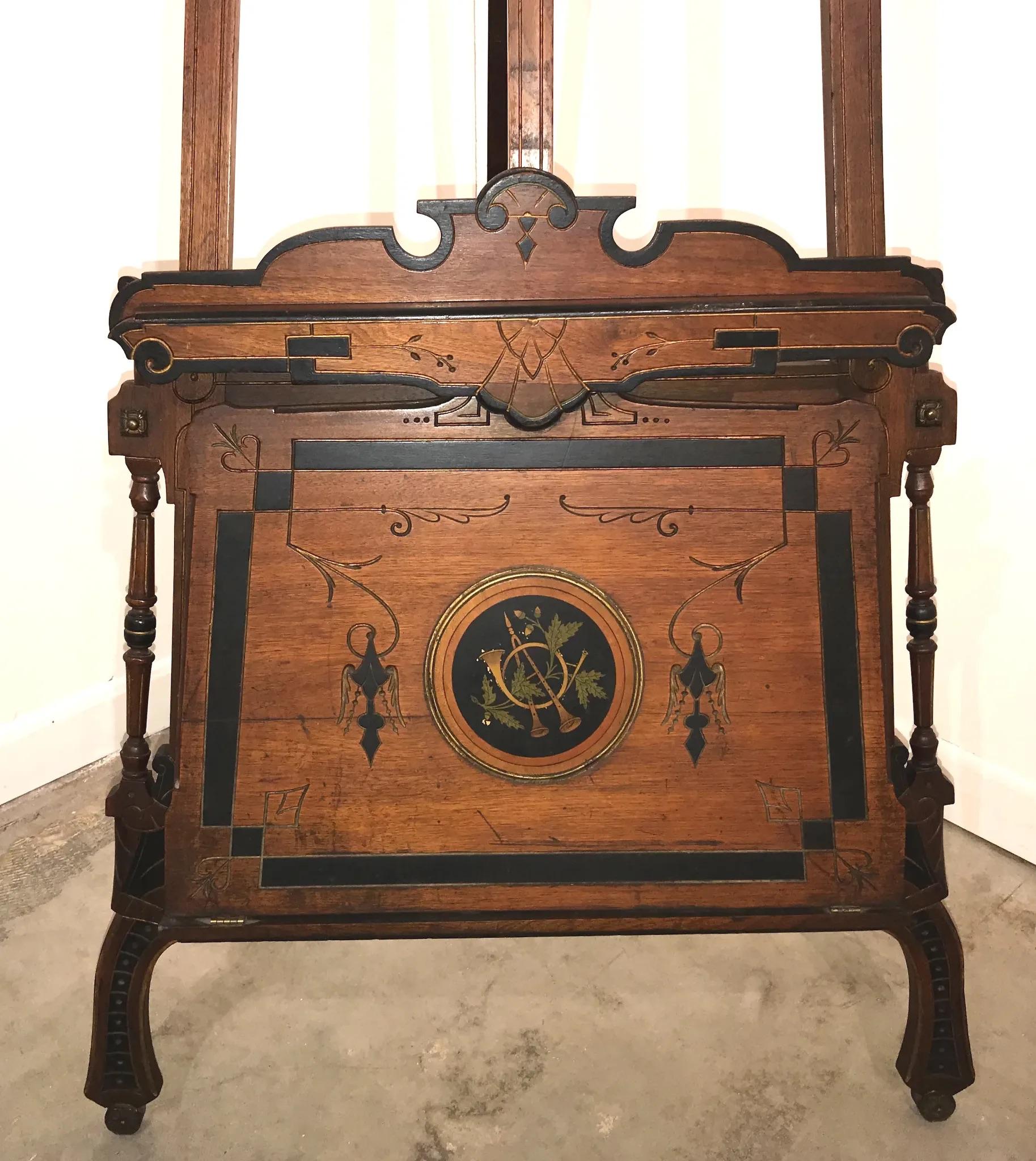 A beautiful example of a Victorian, late 19th century Aesthetic period walnut adjustable painting easel, with nicely carved fold-out portfolio at the base, decorated with satinwood inlaid musical instruments, scrollwork, turned outer support columns