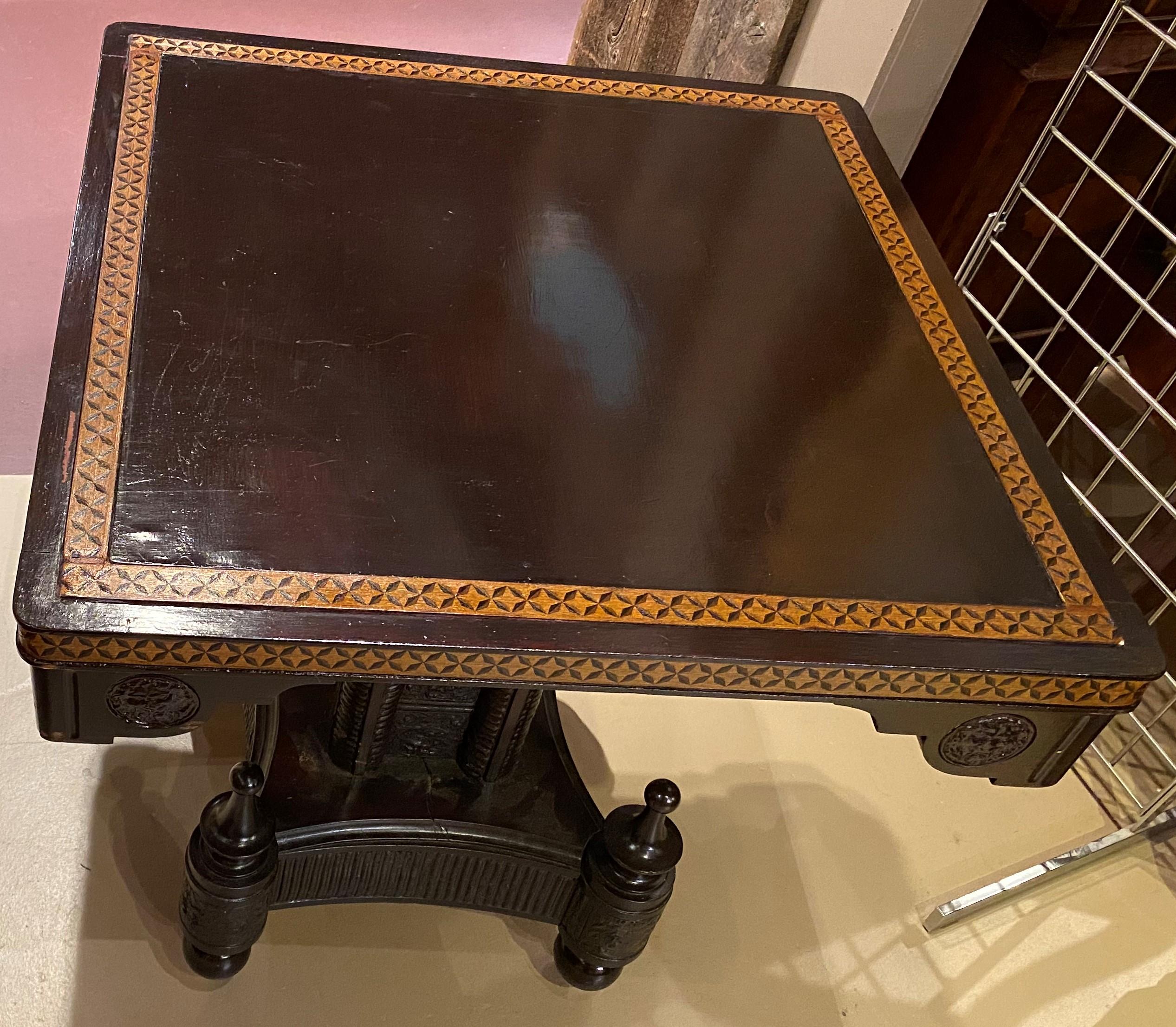 A fine Aesthetic Period tilt top square center table in its original dark finish, with inlaid border top, carved corner decorations, supported by a molded leather lined pedestal and stylized base with four pronounced finials above casters. American