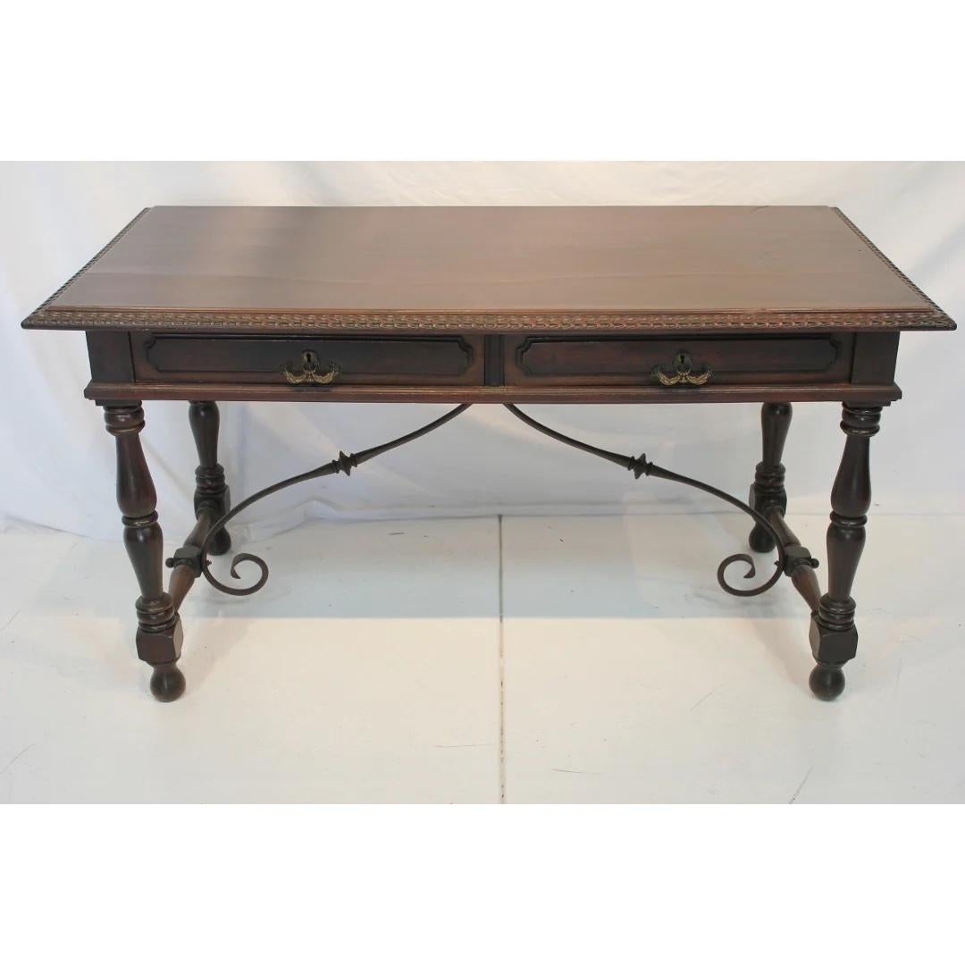 Finely crafted Early 20th Century Spanish Colonial Revival style hand carved mahogany desk with hand forged wrought iron stretcher bars. Two pull out dovetailed drawers with original patinated brass hardware. Hand carved moulding detail around top