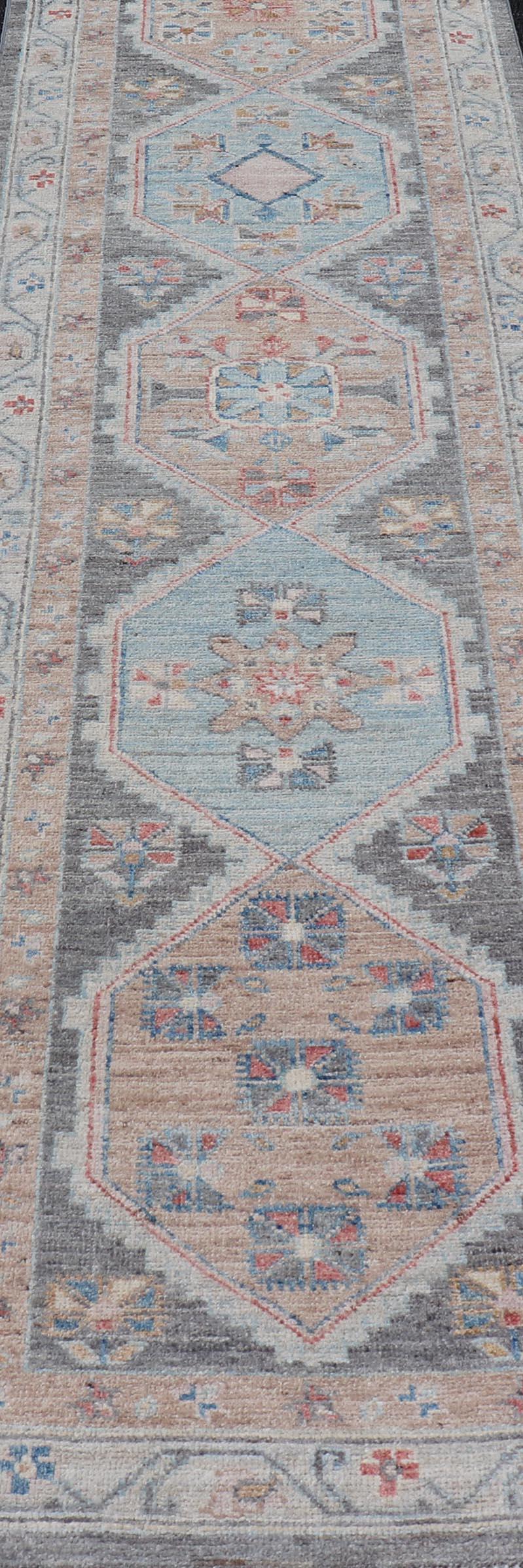 This Hand-Knotted Oushak presents a floral border on top of a dark gray background, accenting colors such as blue, red, and peach. The field displays a creamy orange and a powder blue medallions, showcasing Oushak motifs within. The field also uses