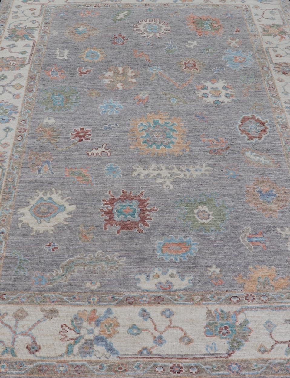 This modern casual floral Oushak designed rug has been hand-knotted in wool. The rug features a modern sub-geometric floral design which is enclosed within a complementary border. The rug is rendered in gray, cream and multi colors, making this rug