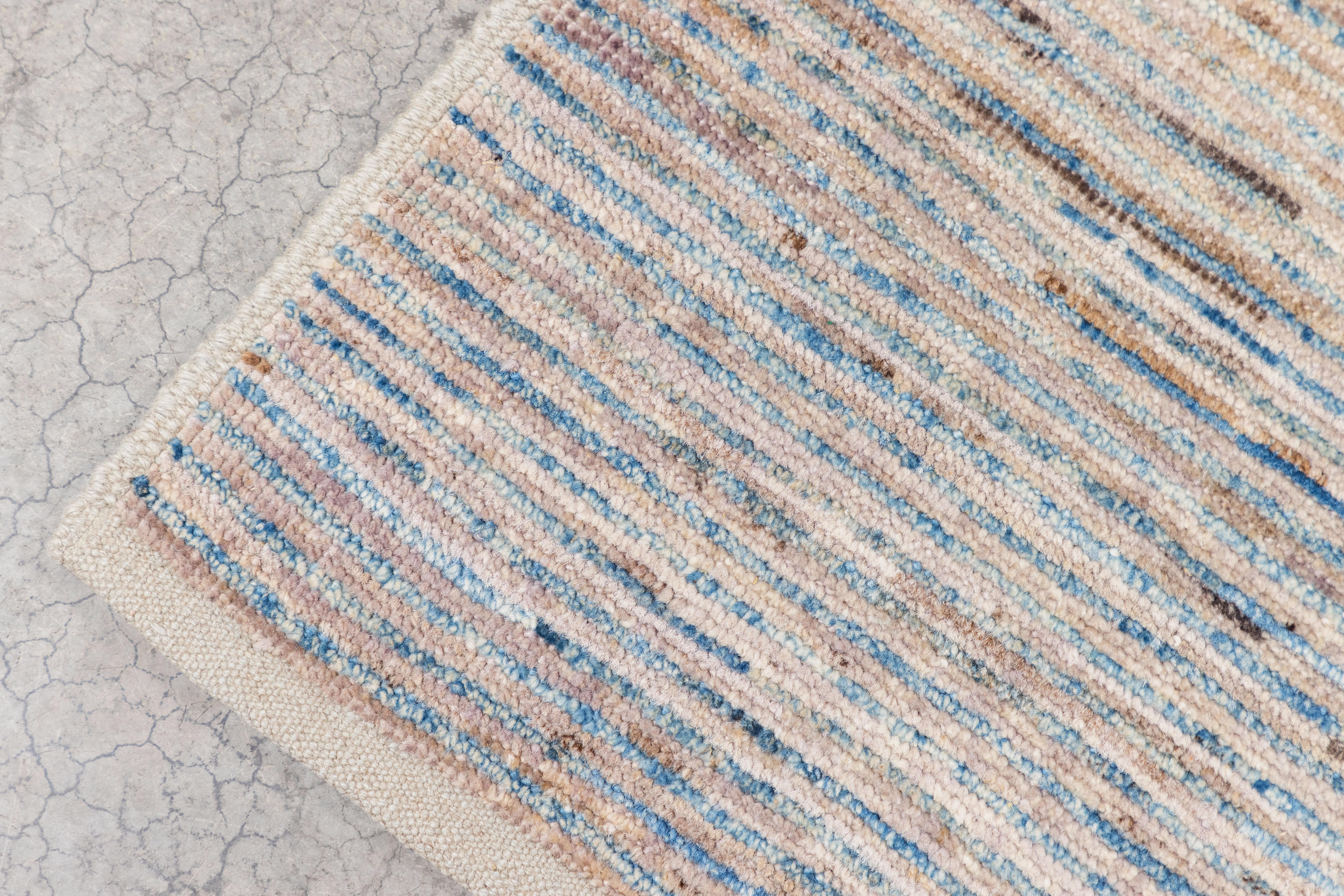 This stunning modern Afghan hand knotted wool rug is made up of an array of subtle blue, gray, beige and cream stripes. It is a beautiful base addition to any room. Measures: 3.5' x 4.8'.
