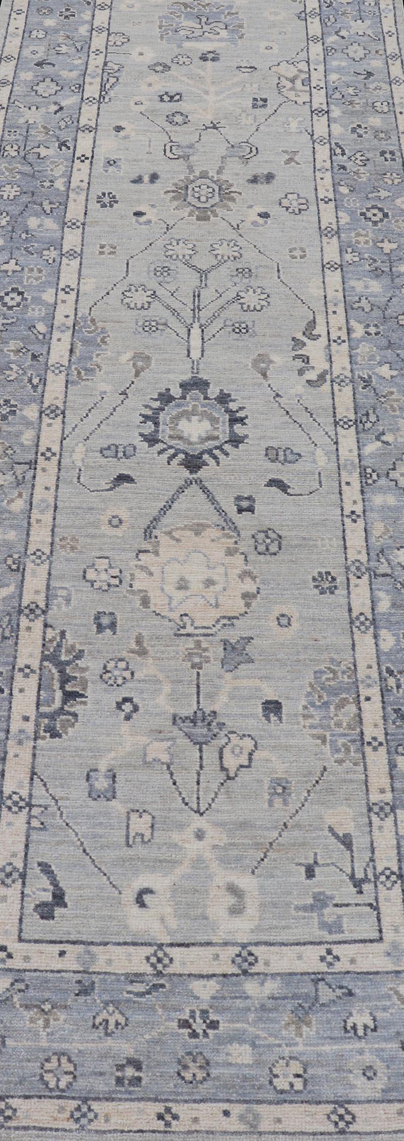 Ce tapis de course conçu par Oushak présente un aspect classique d'Oushak, montrant des motifs floraux brillants et des vignes s'étendant sur tout le terrain sur un fond gris clair. Les couleurs centrales mettent en valeur le taupe, la crème.  bleu