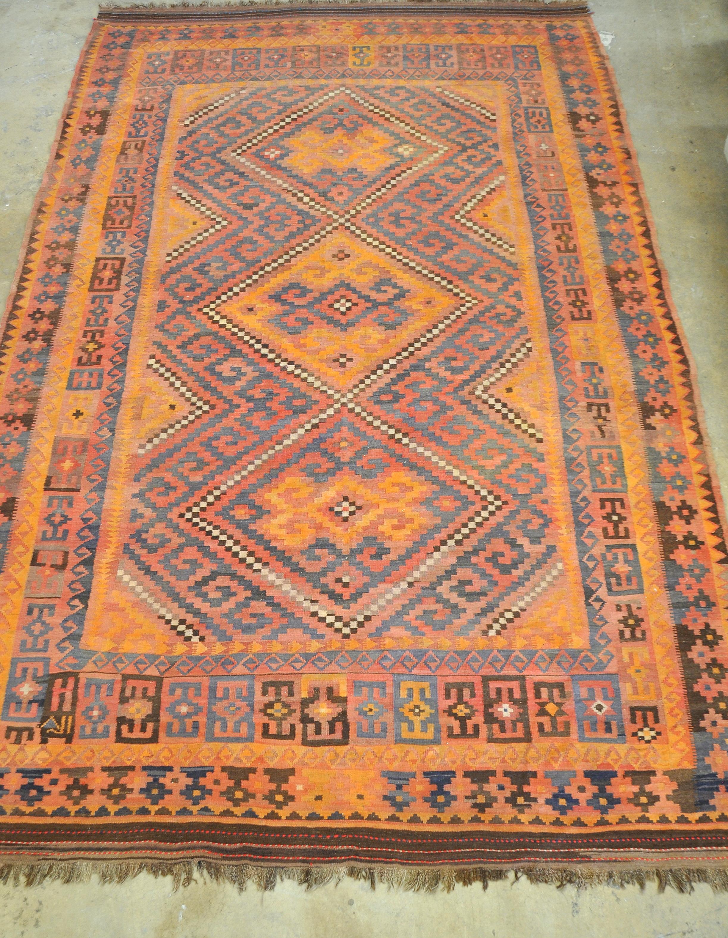An approximately 16 x 10 handwoven Kilim rug made of vegetable dyed hand spun wool. A peachy pastel pink background features yellow, blue, off-white, gray and brown geometric and tribal motifs. Works well with Danish, Scandinavian, Mid-Century