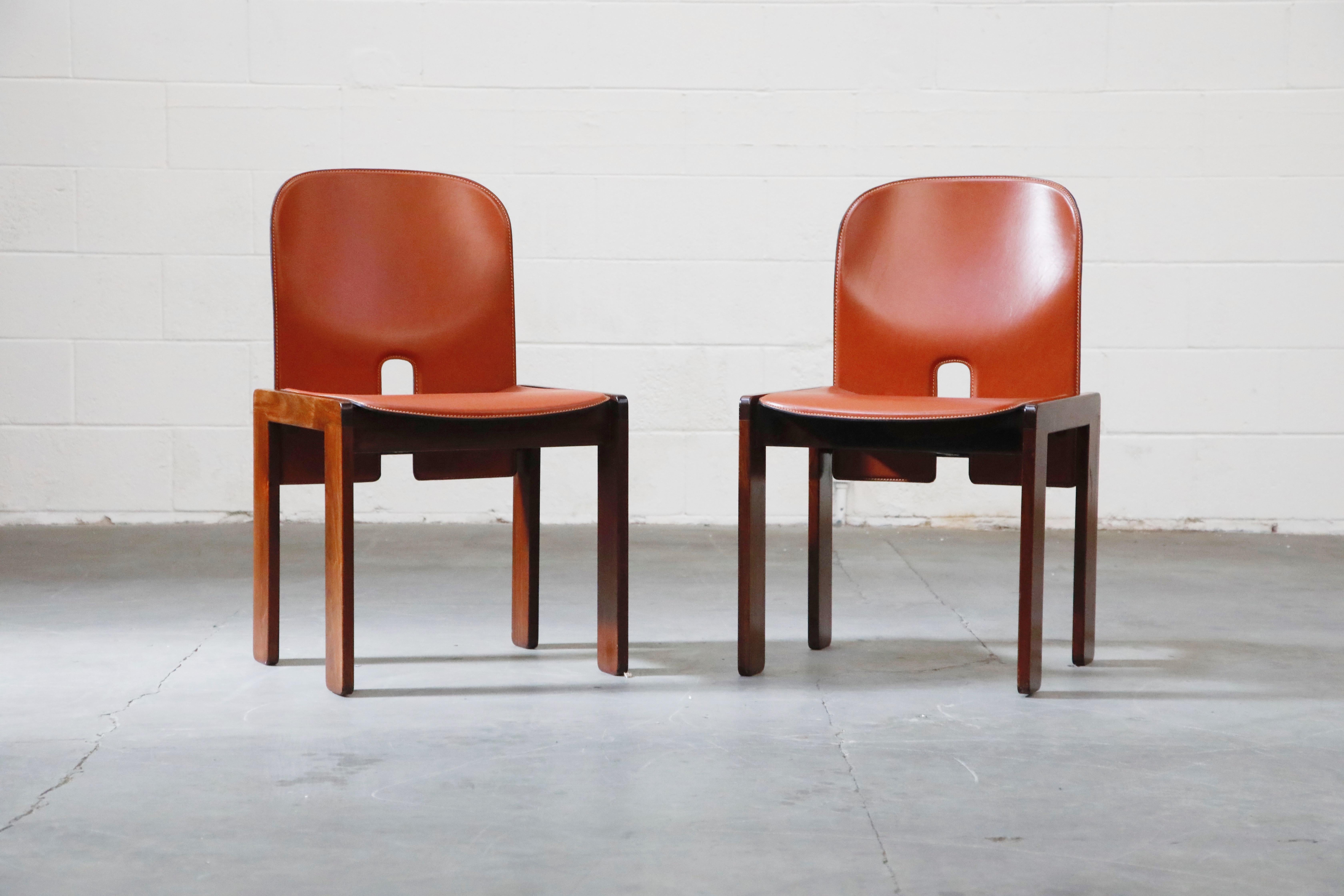 This highly collectible and simply incredible pair of rust-orange colored saddle leather and Rosewood model 121 chairs are by Afra and Tobia Scarpa for Cassina. This particular pair is a perfect collectors set due to several reasons detailed below,