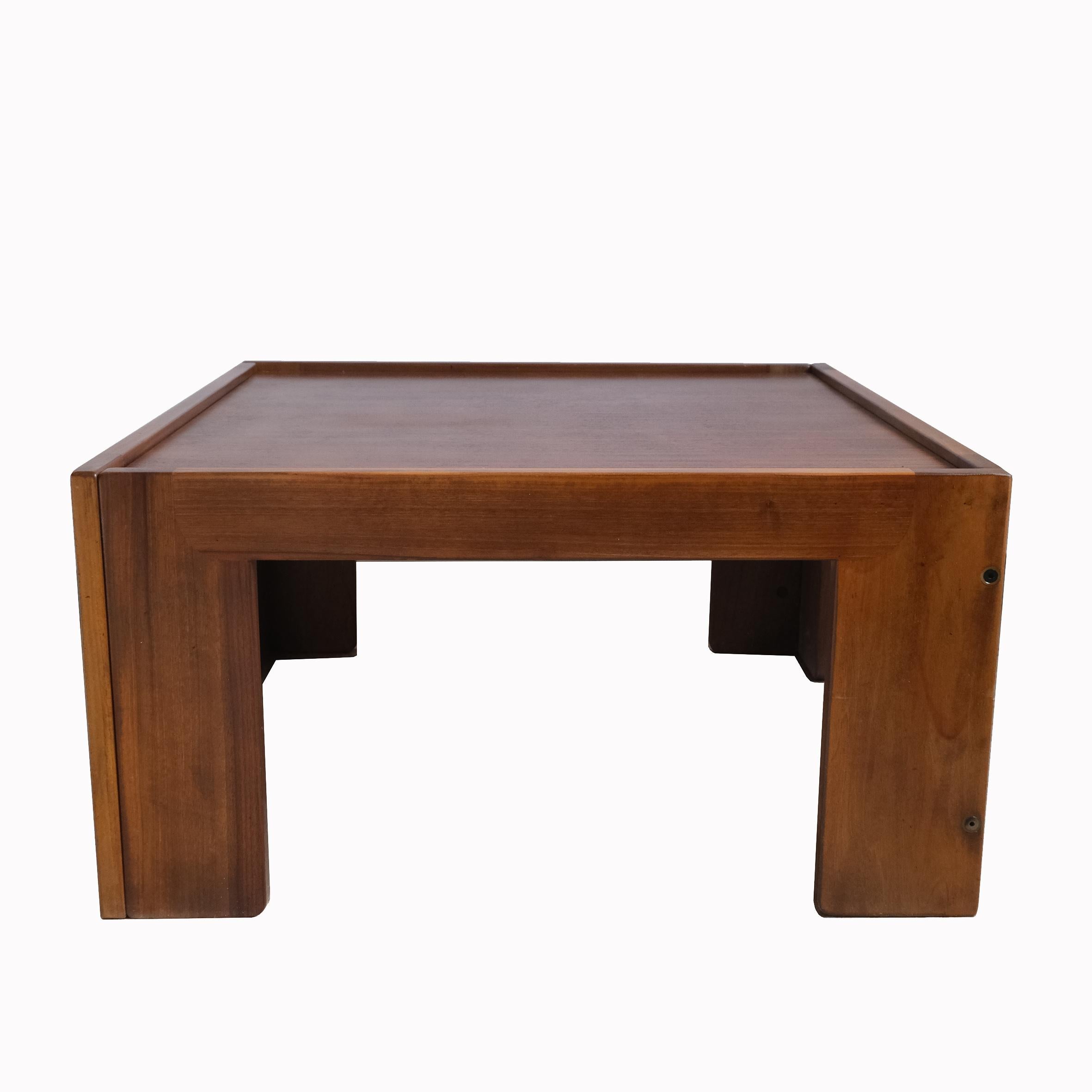 Ein quadratischer, niedriger Tisch aus Nussbaumholz, die Platte ruht auf einem Rahmen, der von vier rechteckigen Füßen getragen wird.
Mit Label 