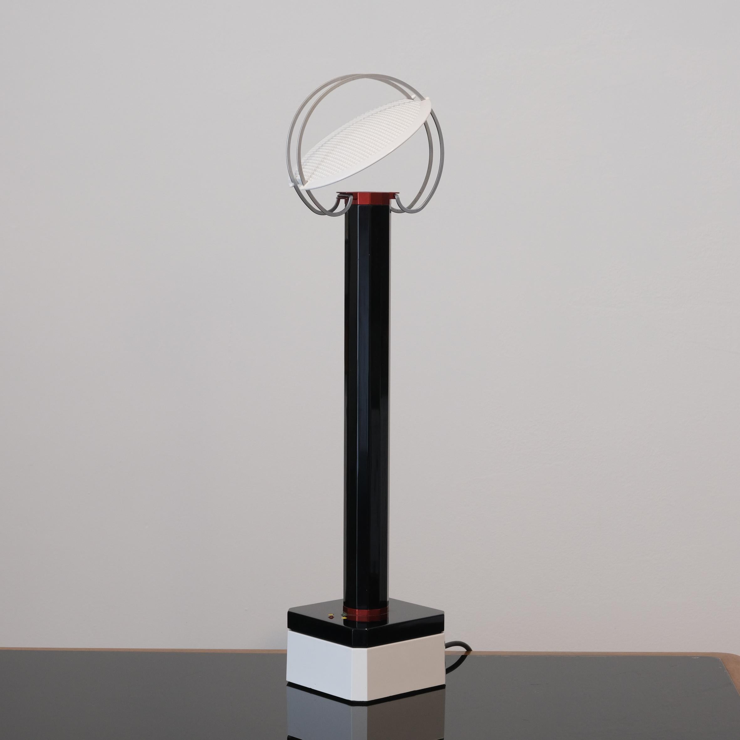 Afra & Tobia Scarpa (1935-2011 & 1935-)

« Perpetua »

An aluminum, steel and plastic portable table lamp, with a  dark blue stem issuing a vertical light reflected by a round mobile shade positioned on two circular steel tracks.
On a square dark