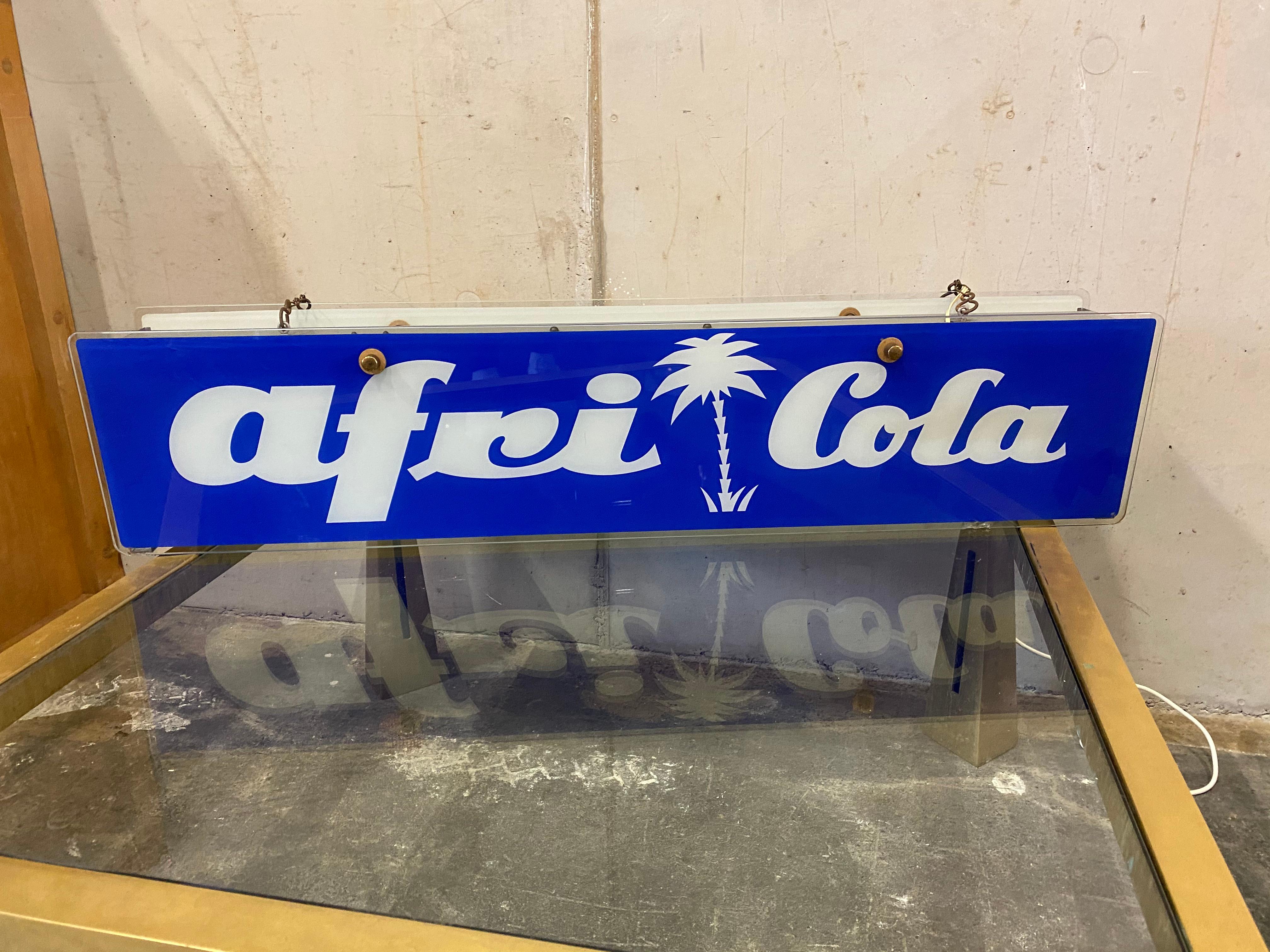 Afri Cola neon sign made of glass and for hanging from the 1950s. Shown is still the old original brand design in blue and white. 
The special feature of this illuminated sign is probably the fact that it is made of glass on the one hand and that