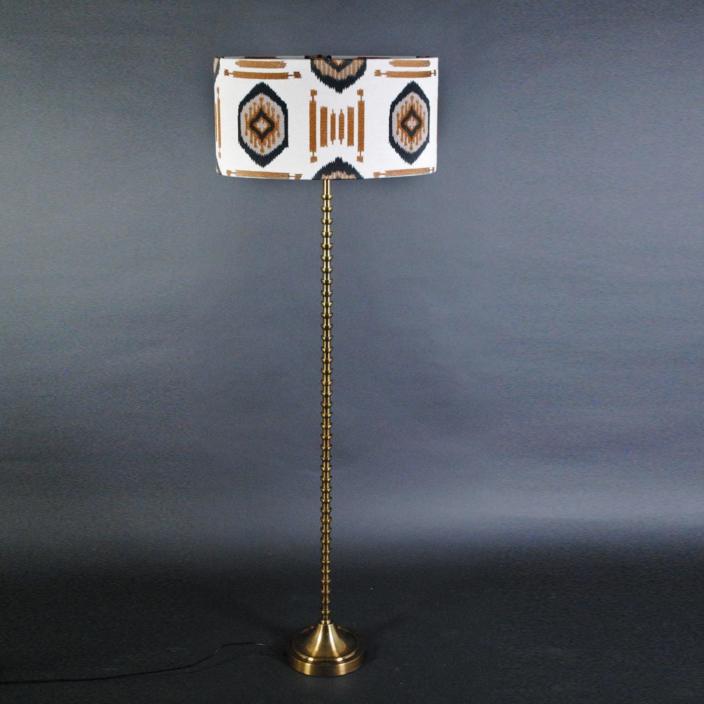 The eloquent inspiration behind this floor lamp immediately recalls tribal cultures, deserts, and African folklore. The streamlined metal frame with a bronze finish features a minutely lathed profile, seductively guiding the eye to the fabric,