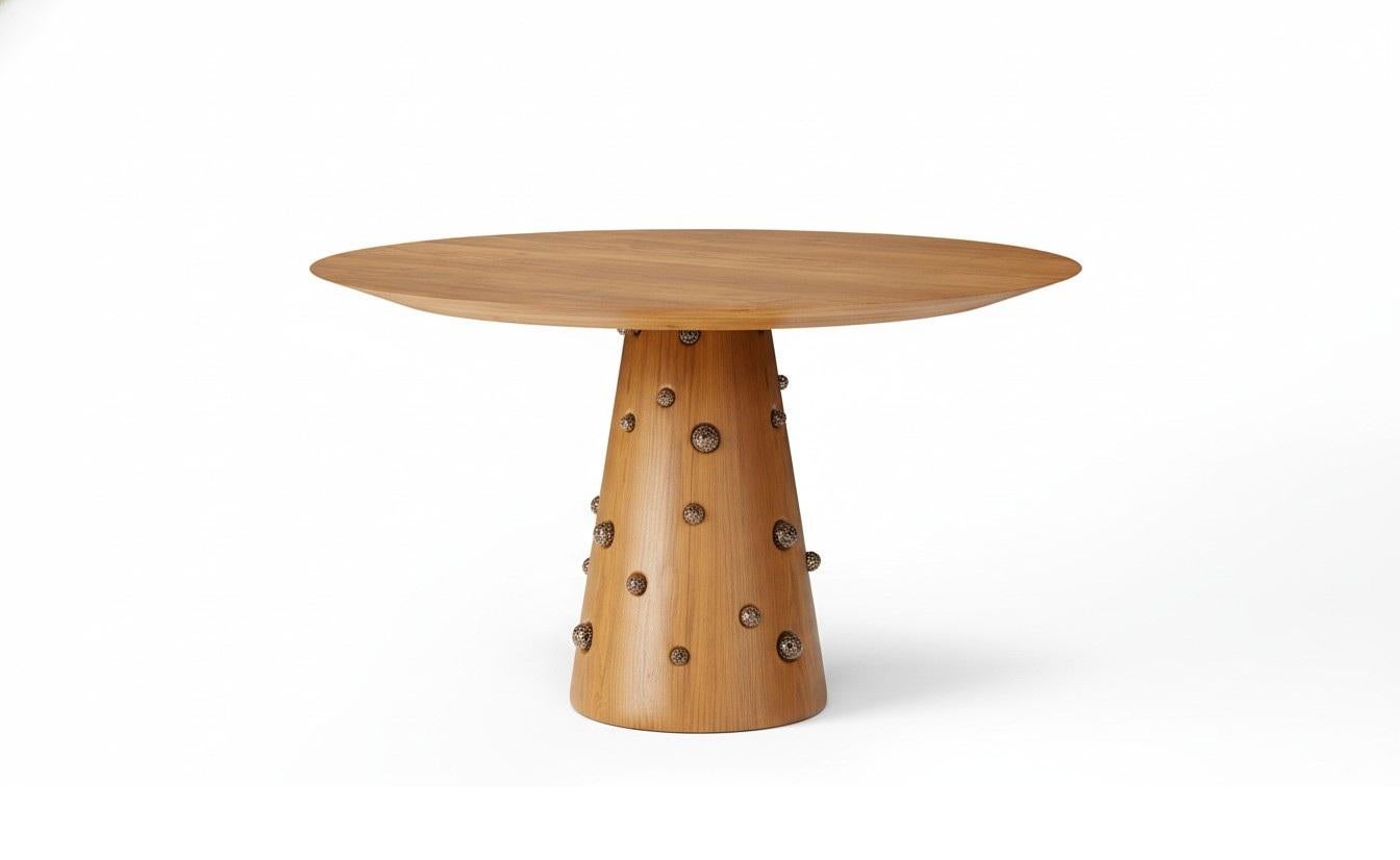 Une table de salle à manger ronde sculpturale qui se distingue par un plateau en bois massif et une base conique enveloppée d'un placage de bois fin. La silhouette est calme et élémentaire, mais richement texturée par des cristaux de pyrite