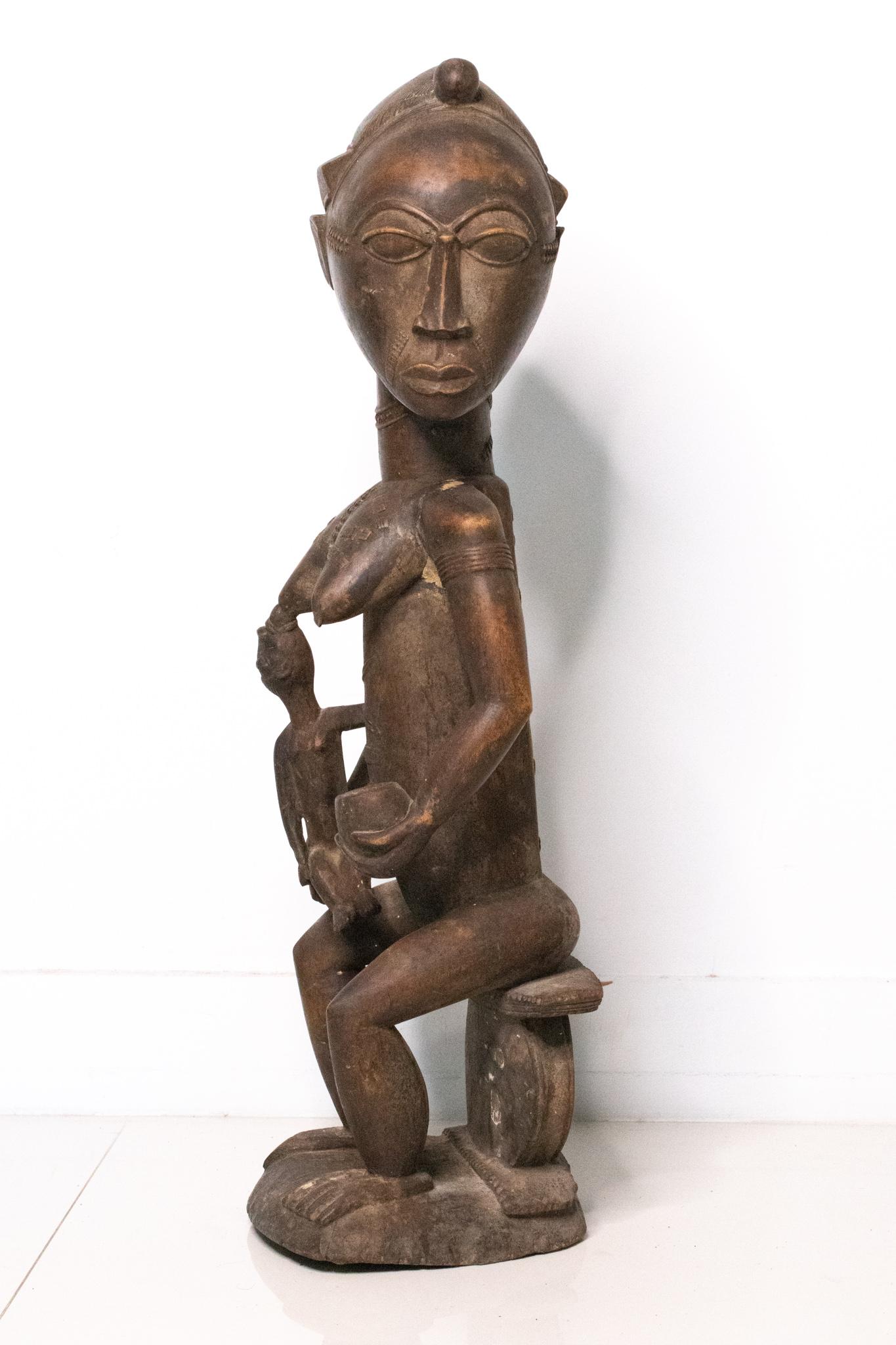Maternity sculpture figure from the Baoule people

Magnificent large sculpture of a seated maternity facing to the left, holding with the left hand an offering vase and breastfeeding a child. This tall sculpture was made in the early 20th century,