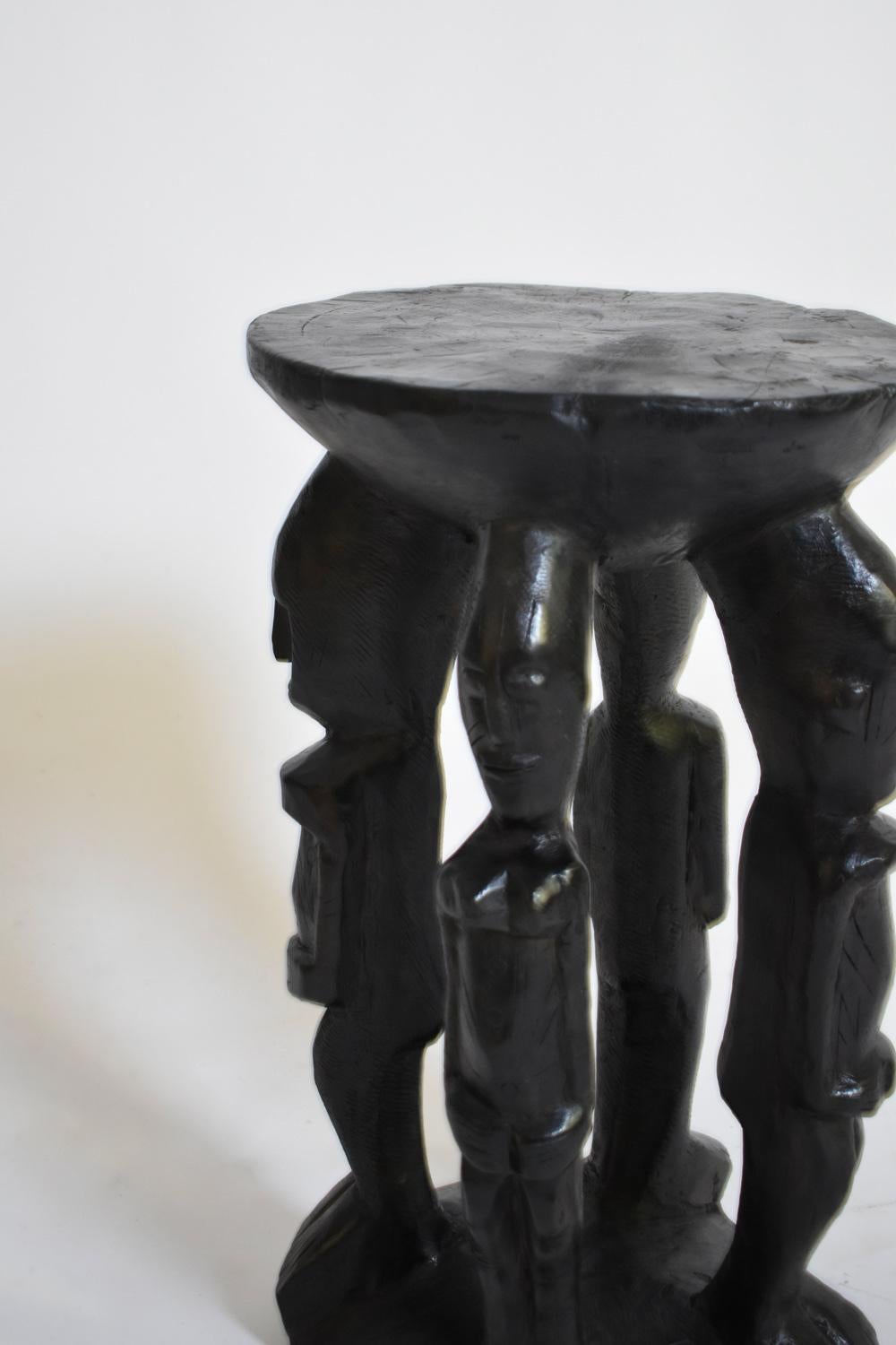 Monoxyl stool or side table formed by four male figures and one female figure made of carved ebonised wood. Africa, 1960s.