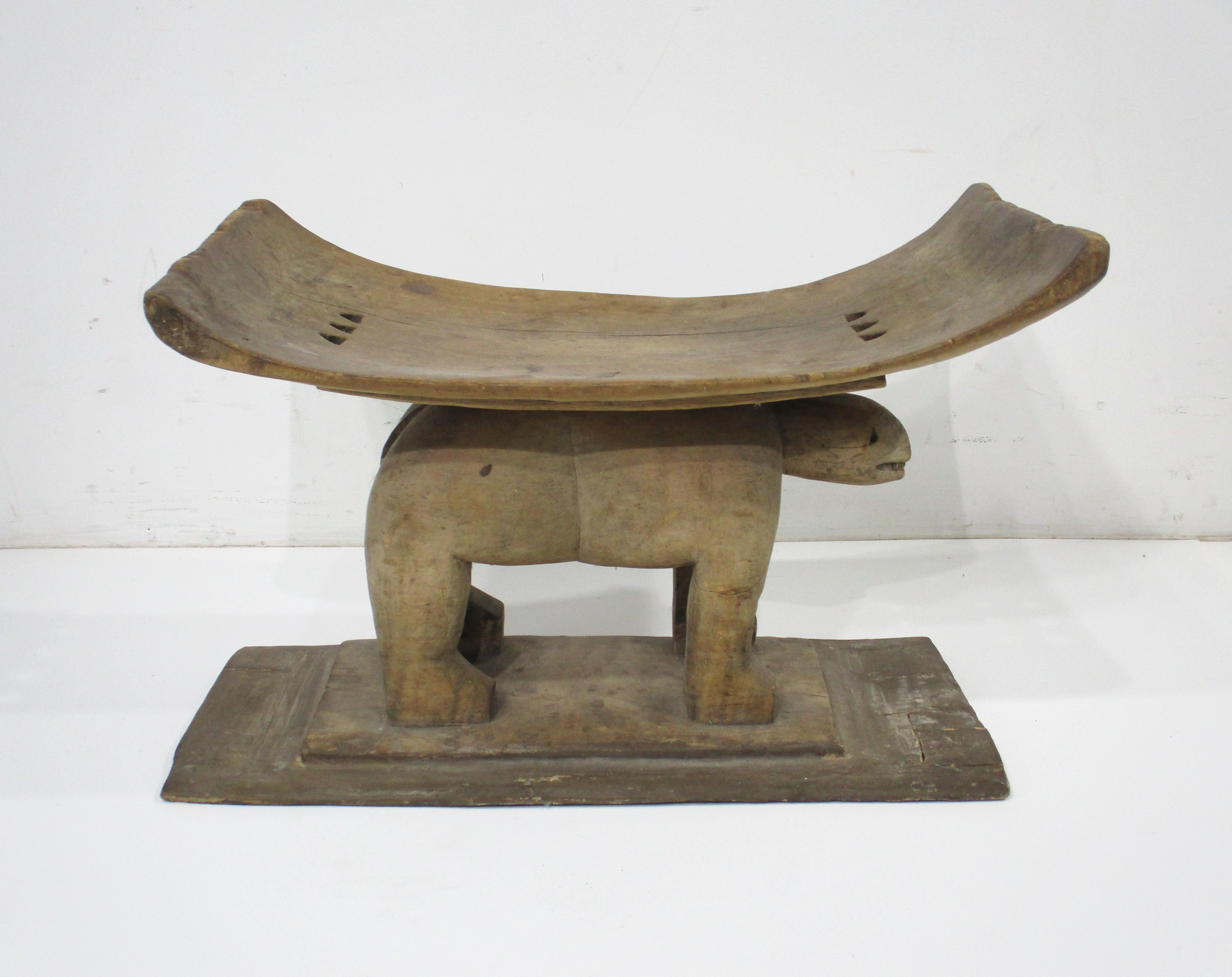 A hand carved primitive wooden Ashanti styled West African Ghana stool or ottoman . The personality of the artistic native carved animal as the base of the curved seat makes this unique , functional and a fun object in any room or mixed with any