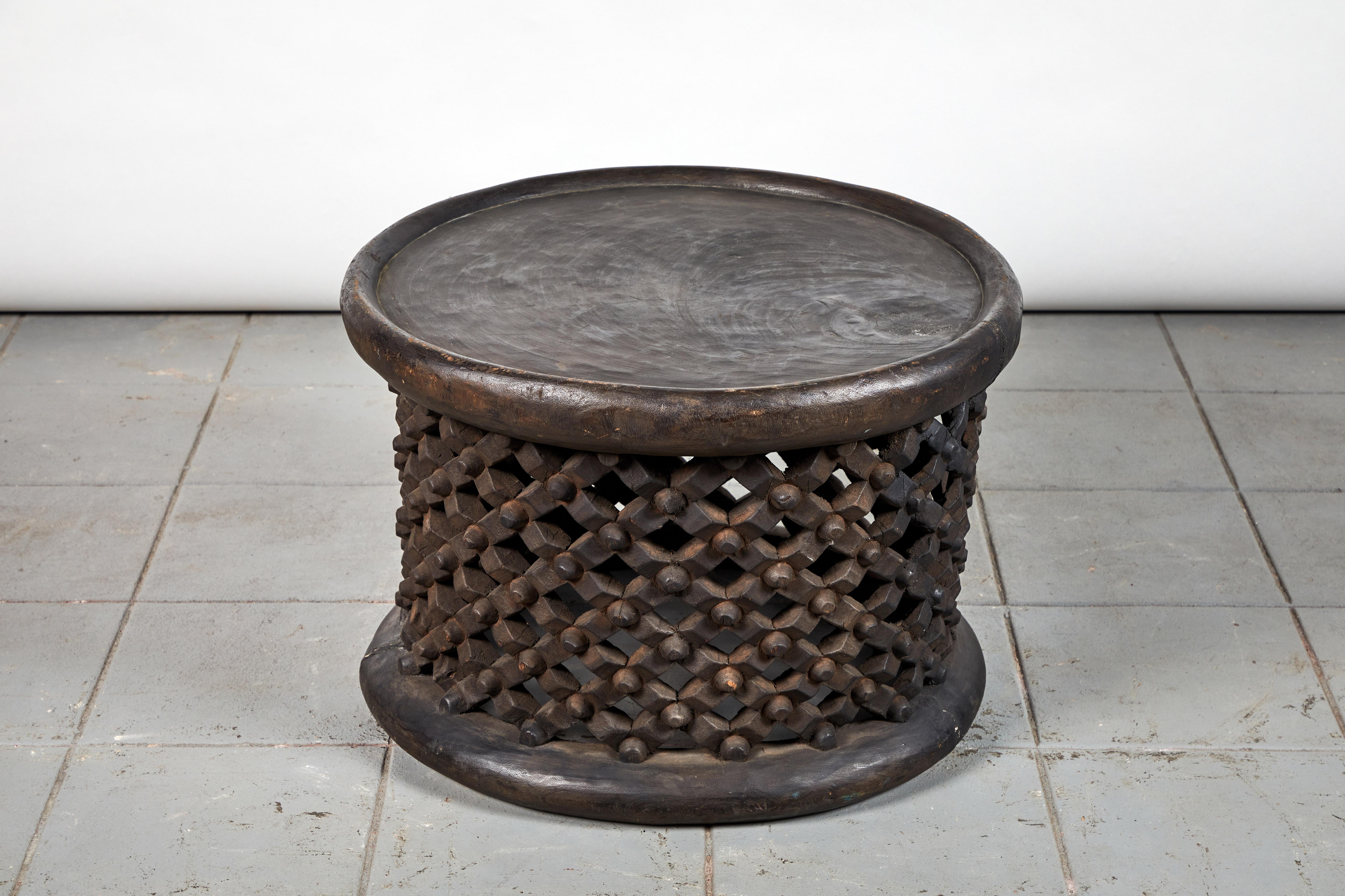 A Cameroon wood drum table with pierced and carved lattice base. The size and height is great to use as a stool, side table, or occasional table. The lattice work on the bench is in good condition, however, due to the inherent nature of solid wood