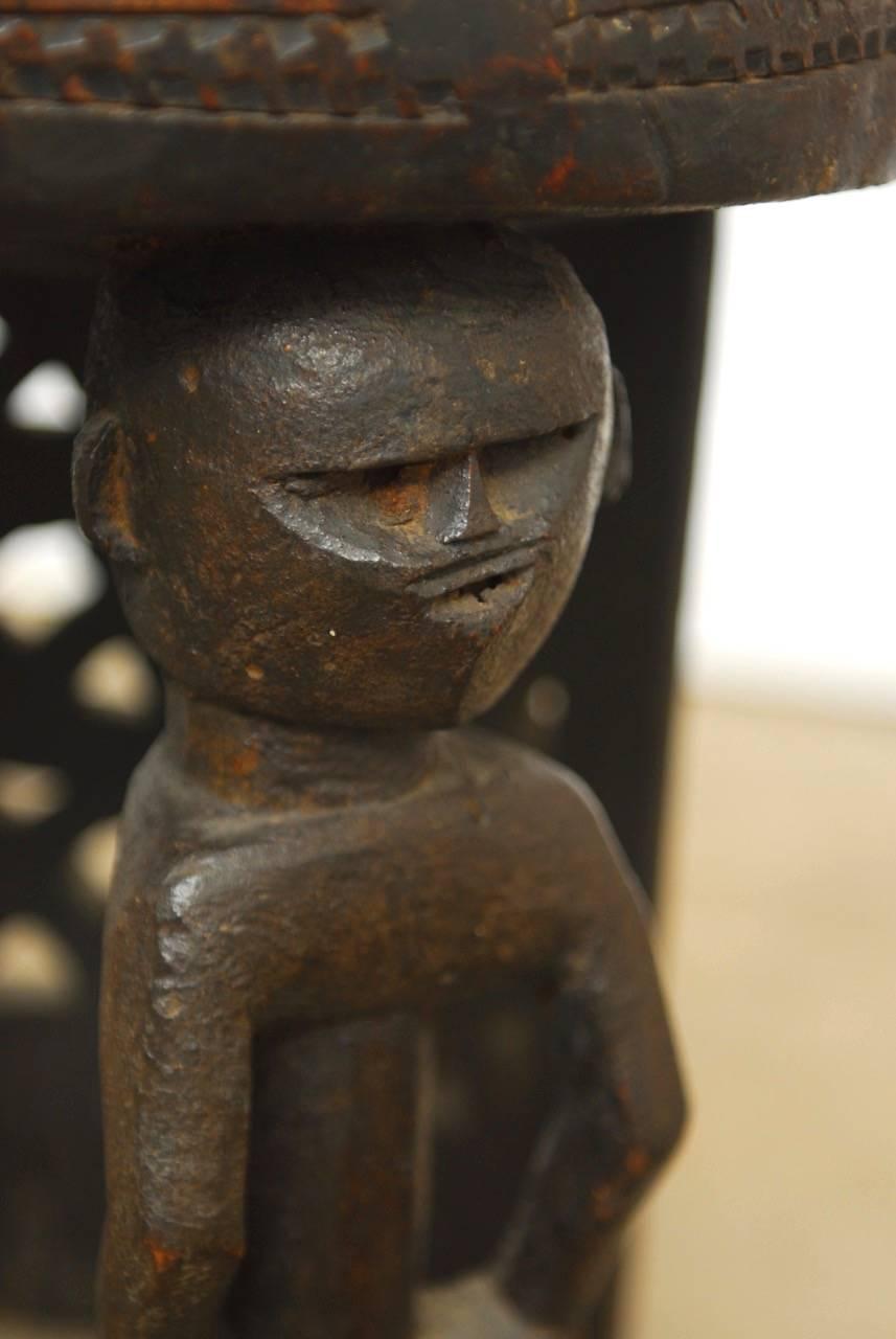 Primitive African carved tribal stool featuring two figural legs in front and a rear support with a geometric design fretwork pattern. The stool has a nearly ebonized finish with a beautiful patina. Strong and solid carved from a single timber. The