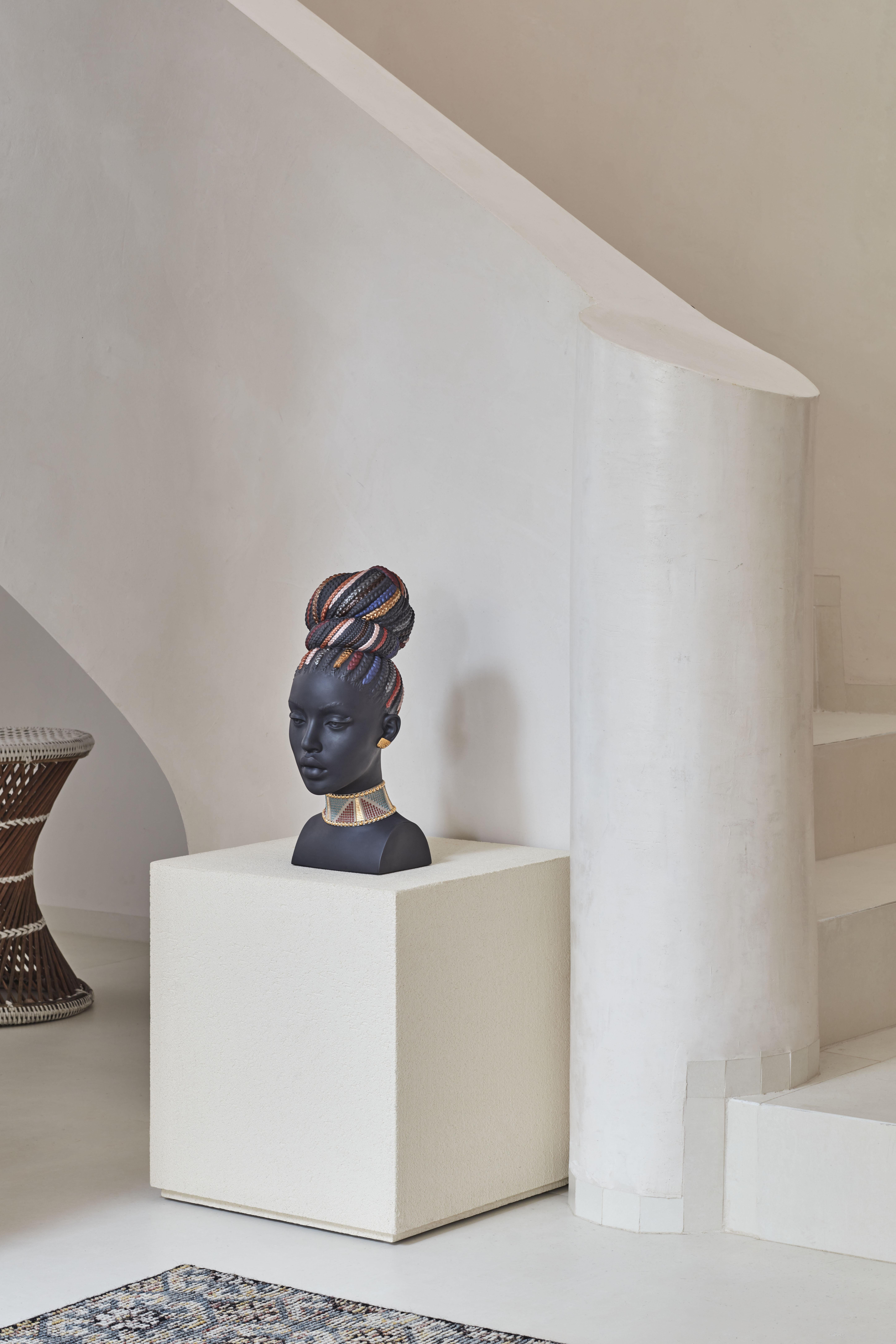 Made in matte black porcelain, this bust of a woman borrows its inspiration from the symbolism and intense coloring of African culture. The serene facial features, masterfully sculpted, are rounded off with a decoration using luster and metallic