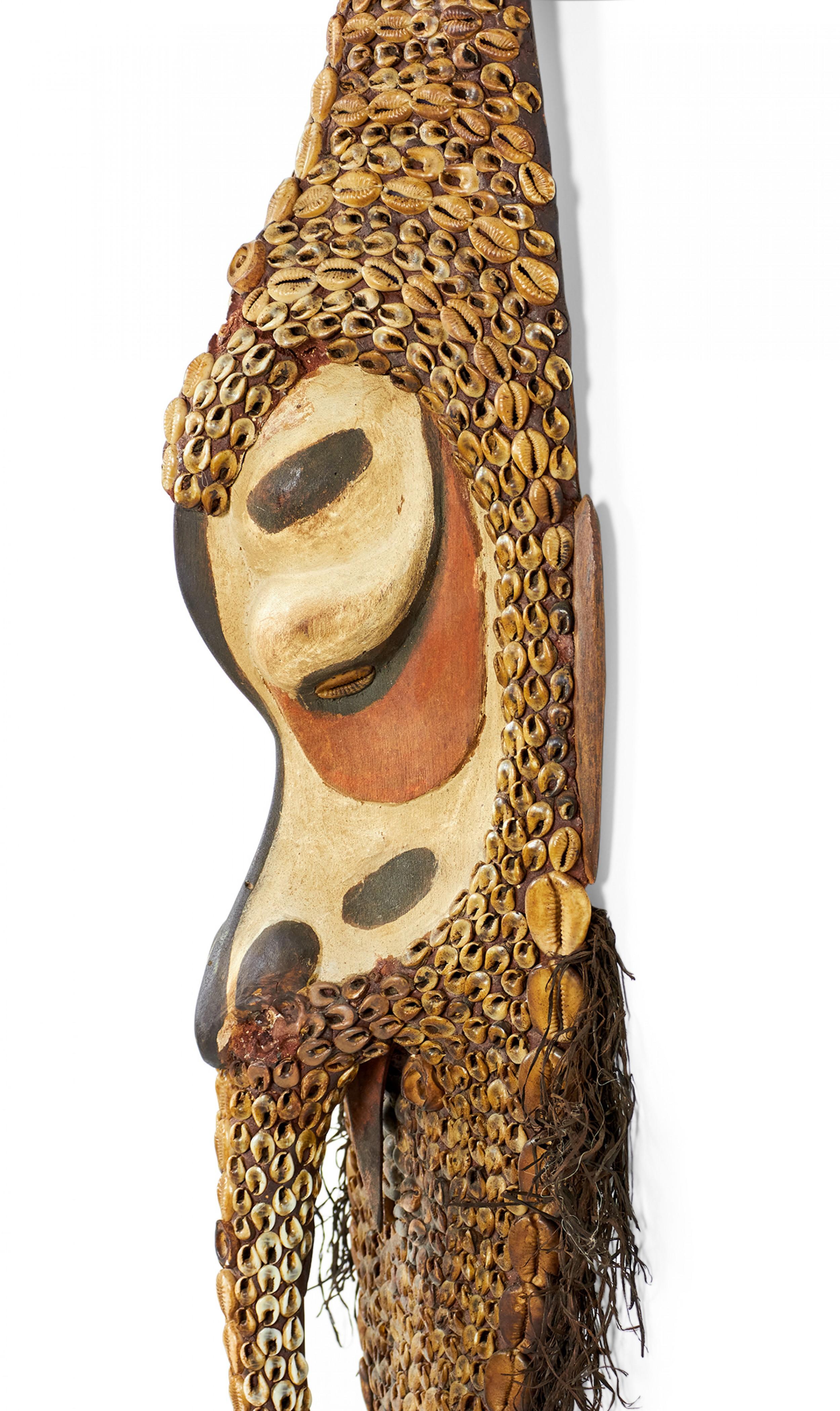 African (possibly Liberian / Dan-Style) carved wooden mask decorated with an intricate pattern of cowrie shells along its outer face and long beak with orange, black and beige painted accents and a root fiber beard.