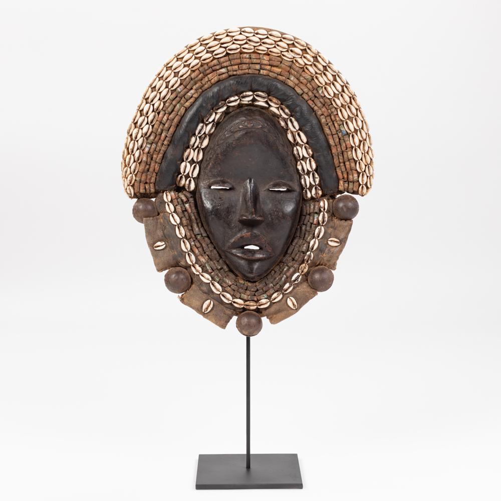 African Dan Yakuba Guard Mask Small Shells and Bells from the Ivory Coast 1970s
Female wooden mask with rich decoration of textile elements, small shells and ceramic beads.
The mouth, nose and eyes are highlighted and a carved band runs across the