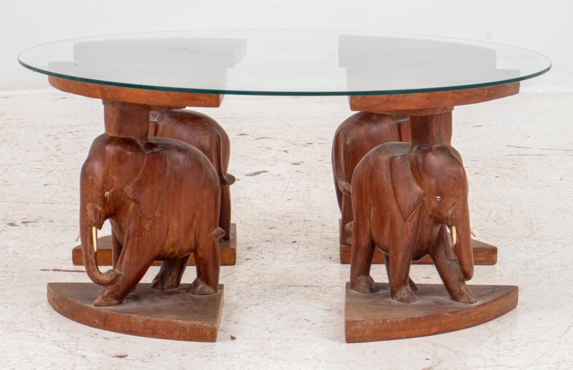 The African coffee table features four elephant-carved wood legs and a round glass top. Its dimensions are approximately 14 inches in height and 30 inches in diameter.




