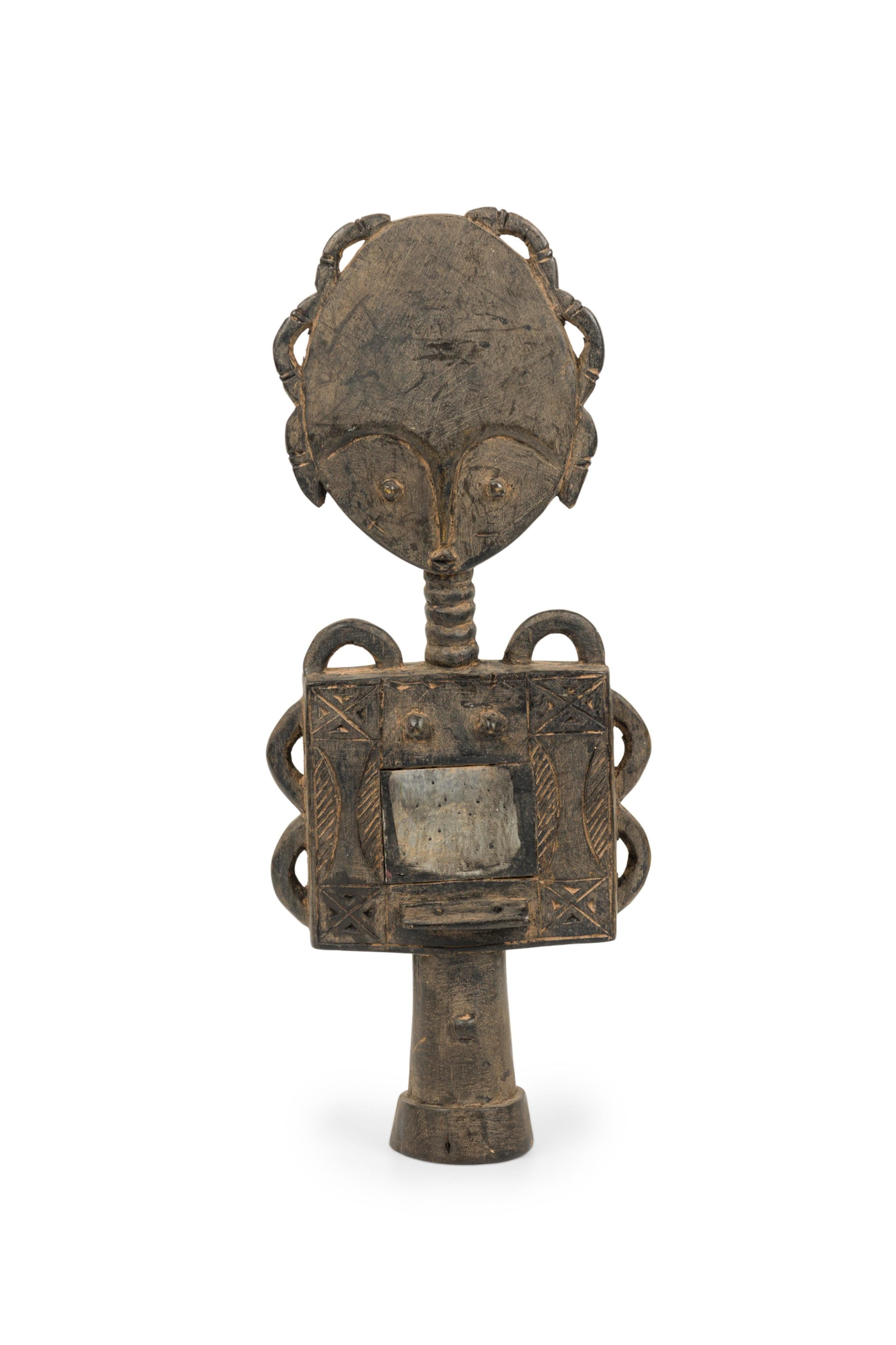 Vom Ashanti-Volk handgeschnitzte ghanaische Fruchtbarkeitspuppe aus dem 20. Jahrhundert, die eine Figur mit übertriebenen Augenbrauen, schlangenartigen Formen über Kopf und Oberkörper und einem gespiegelten Unterleib, umgeben von geschnitzten