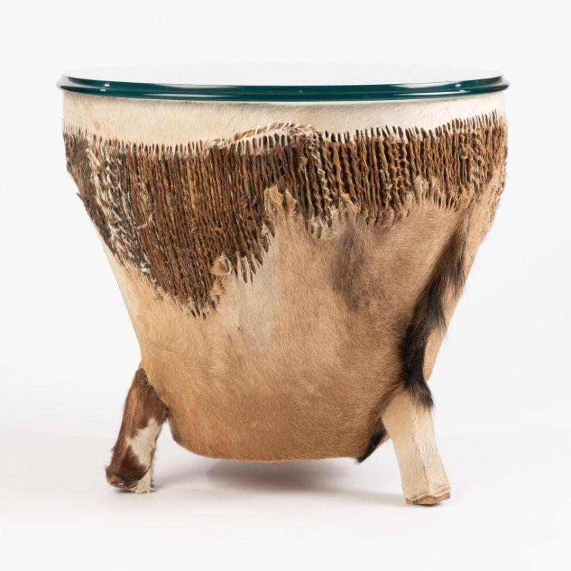 West African style Djembe drum table on tripod feet covered in hair-on-hide goat skin. The drum top has been fitted with a conforming circular 1/2” glass top with ogee edge.
African, mid 20th century.