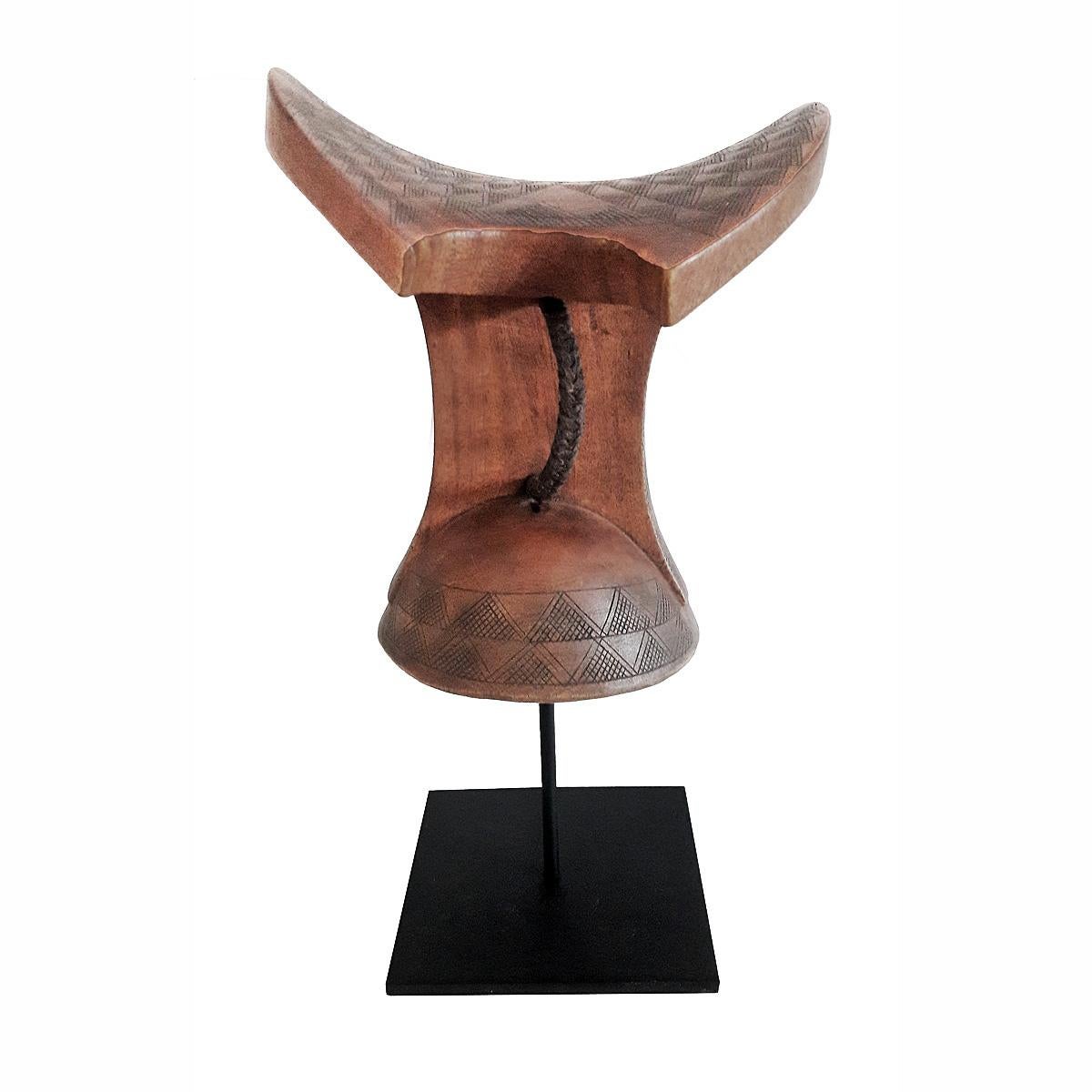 A headrest or stool, hand carved out of a single piece of teak wood, and decorated with traditional carvings, with a braided leather handle from Ethiopia, late 20th century. Mounted on a black metal stand.