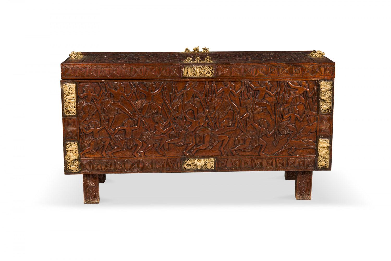 Cassapanca africana contemporanea (XX secolo) in legno intagliato con cerniera, con intagli figurativi sulla parte superiore e sui lati e intagli geometrici lungo lo schienale e il bordo del coperchio, con figure in ottone, che poggia su quattro