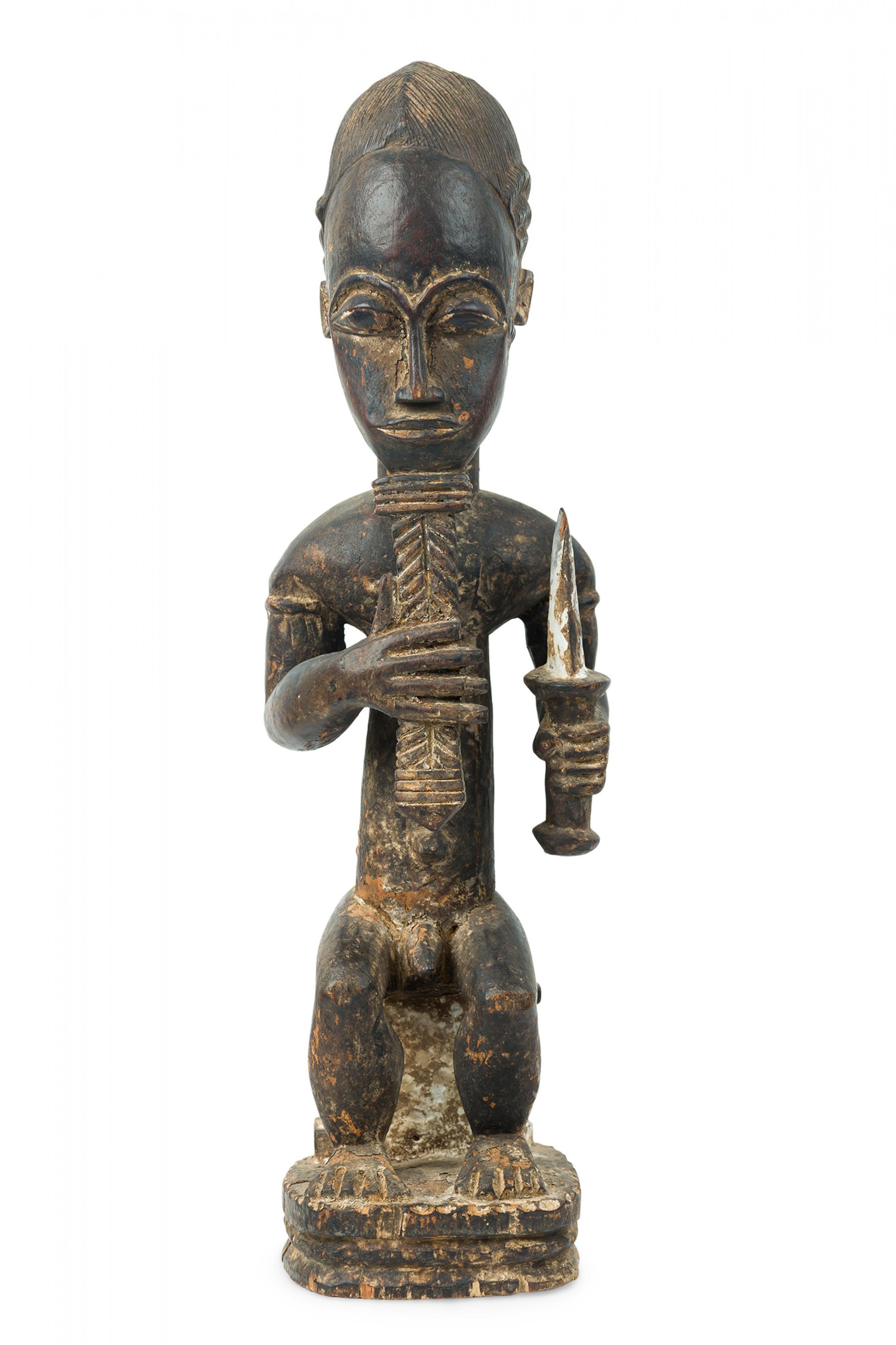 Costa d'Avorio africana 20° secolo, legno intagliato Baule, figura di divinatore in trance seduto con capelli incisi, che impugna un pugnale nella mano sinistra e si accarezza la barba con la destra.

Usura della finitura, alcune perdite,