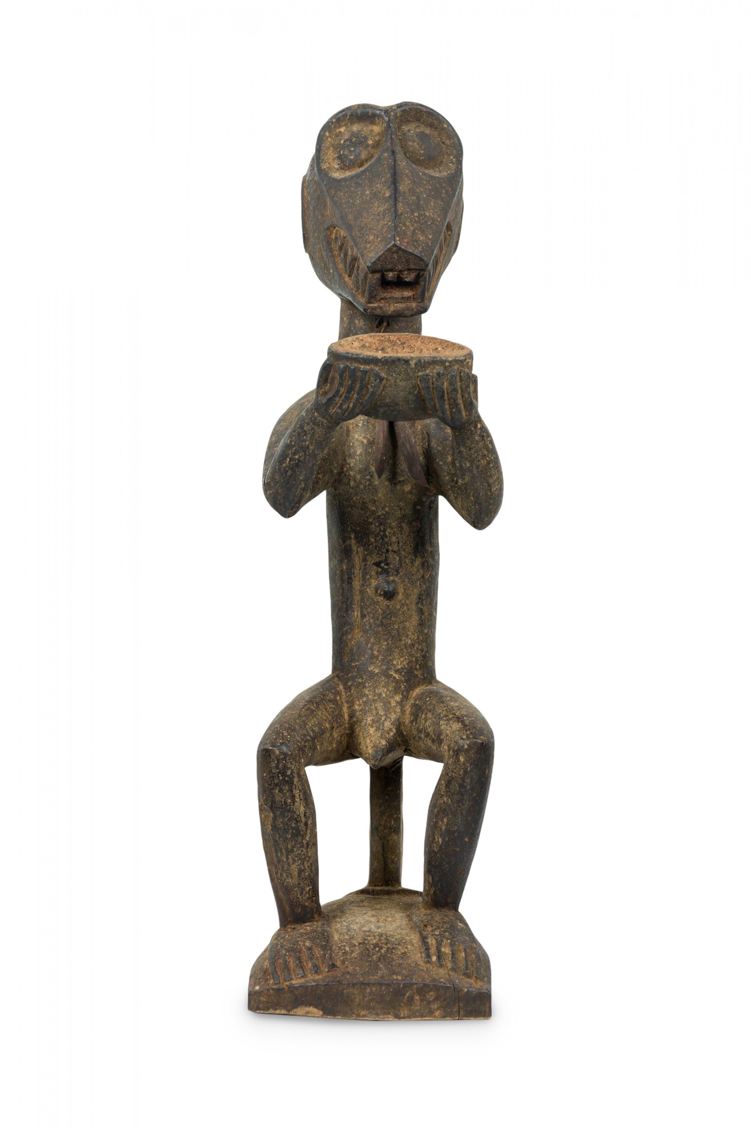 Figura di scimmia Baule Mbra in legno intagliato della Costa d'Avorio del XX secolo, seduta con una collana di corde e con in mano una tazza o una ciotola.  (Letteratura: pag. 238, Baule: African Art, Western Eyes di Susan M. Vogel) (Articolo