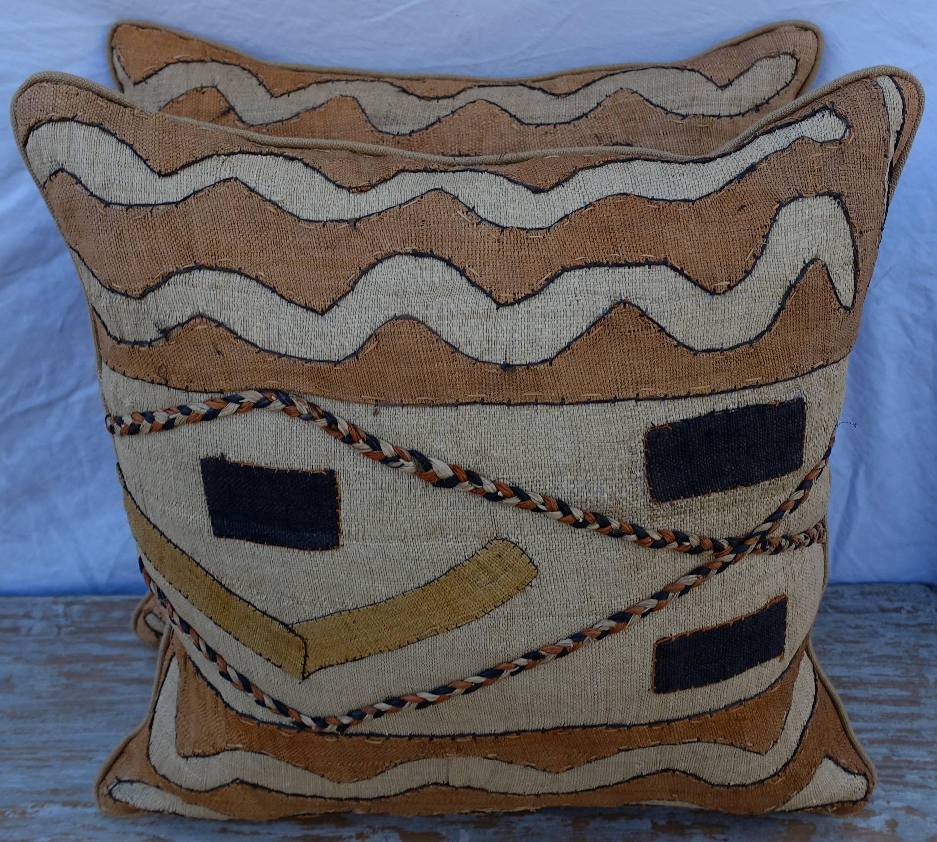Pair of custom African Kuba cloth pillows made with woven raffia fronts and wheat colored linen backs. Self welt detail, sewn closed.