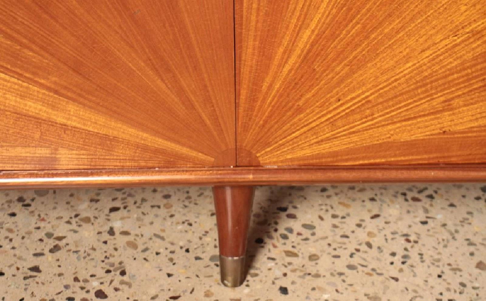 This Mid-Century Modern side board is made of African mahogany, featuring 6 doors with starburst design. The interior features glass shelving and drawers in the center cabinet. Gorgeous piece.