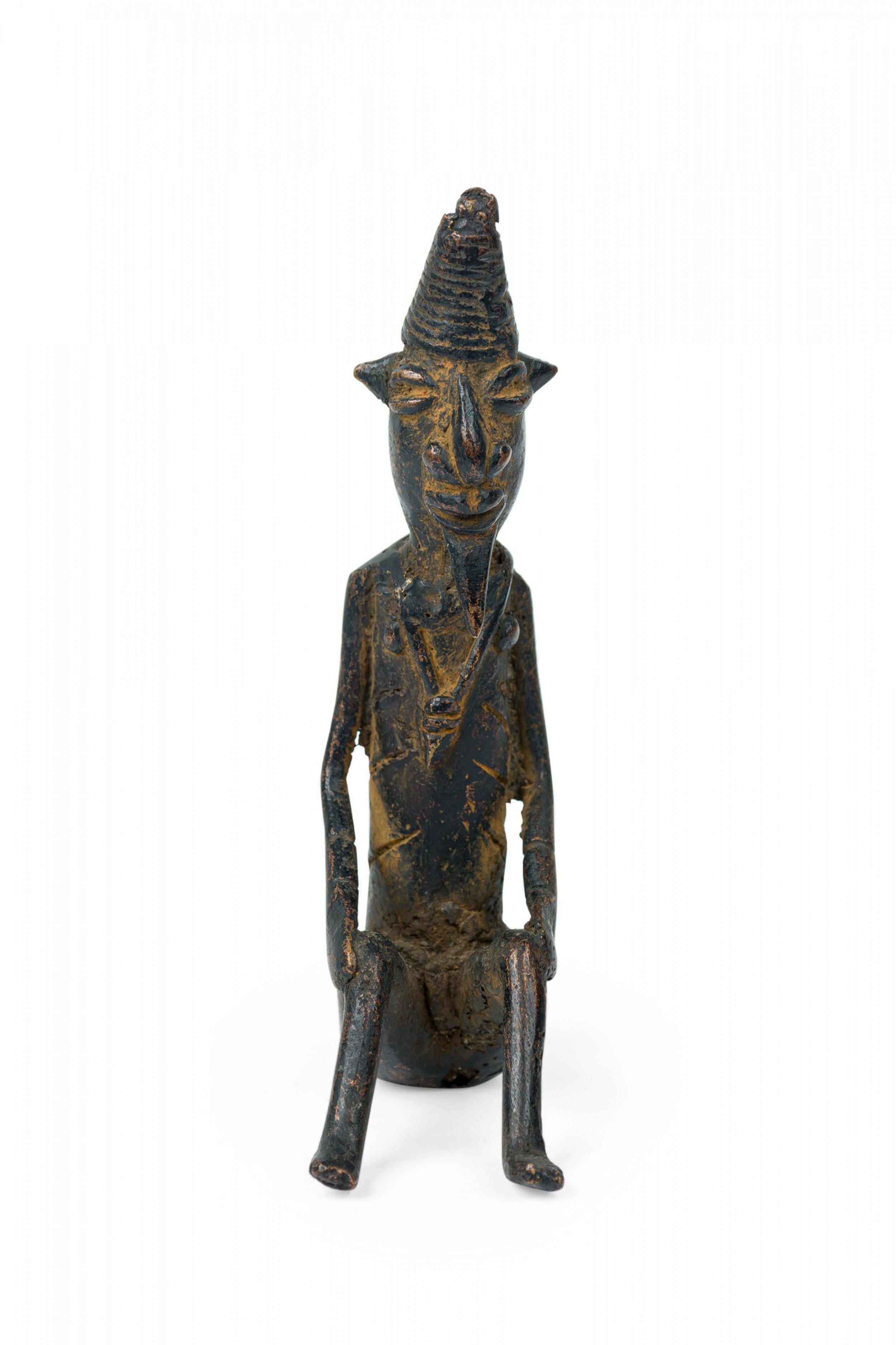 Afrique Mali Fin du 20e siècle bronze Dogon figure masculine de vieillard de village assis, réalisée avec le procédé de la cire perdue, portant un chapeau conique, une amulette, une expression faciale souriante et une barbe stylisée.

Usure de