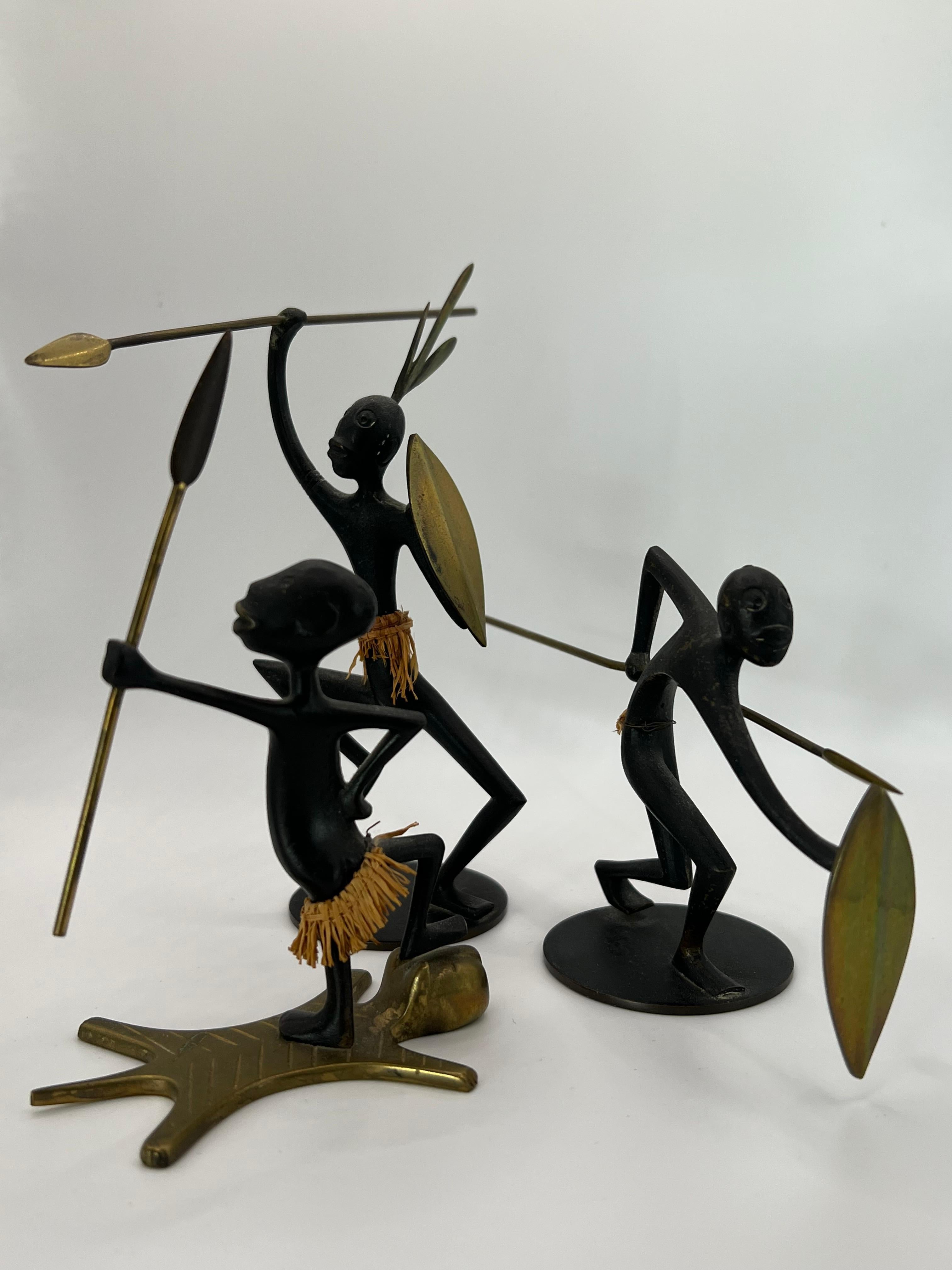 A beautiful group of three (3) Mid-Century, black-patinated bronze and brass sculptures, showing stylized African native warriors with shields and spears . Designed and executed by Karl Hagenauer, Werkstätte Hagenauer. In very good condition with