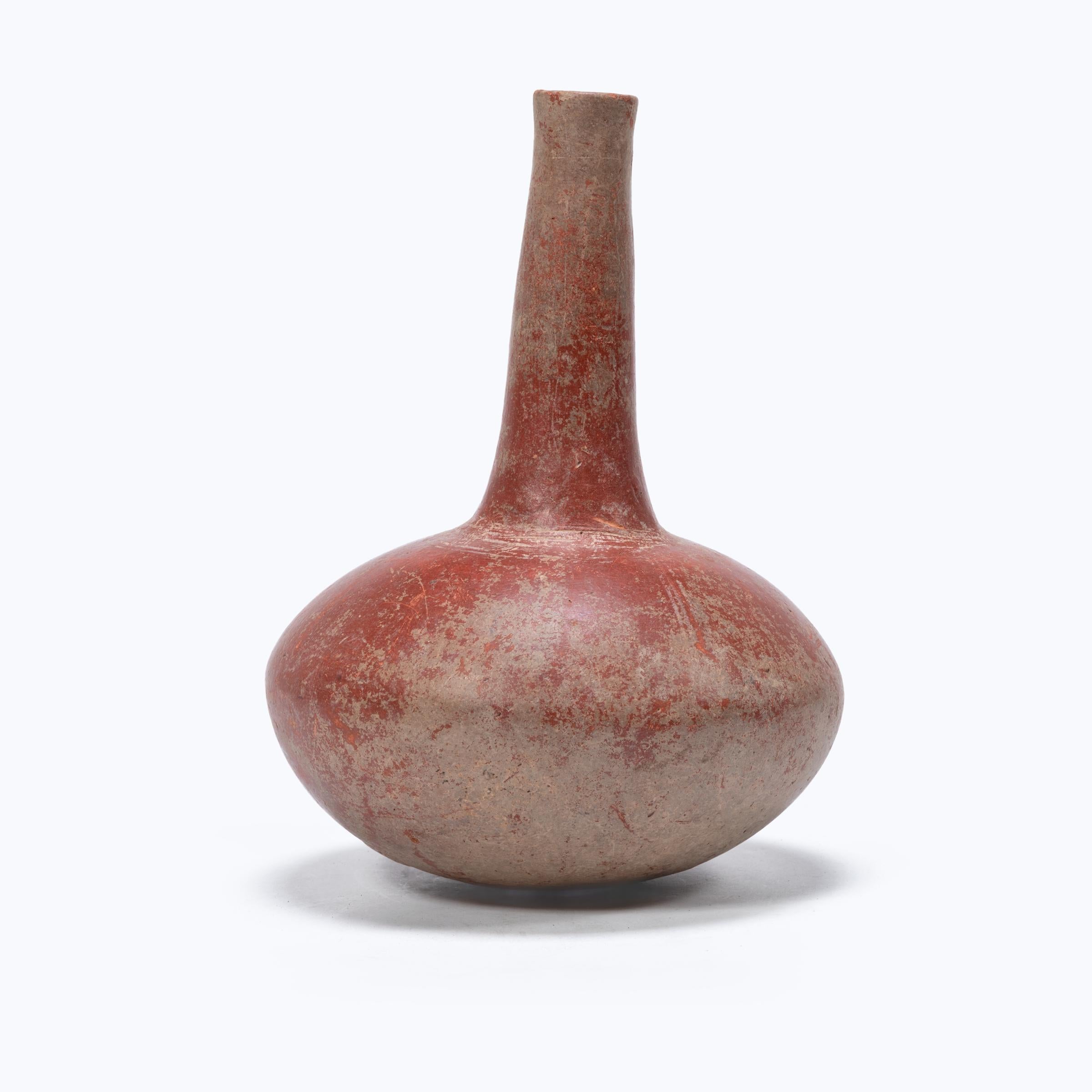 Covered in a beautifully worn red clay slip, this hand-formed African vessel has a dramatic silhouette of a squat, ovoid body and a long, narrow neck. Subtly etched crosshatch patterns encircle the base of the vase's long neck, and vertical lines