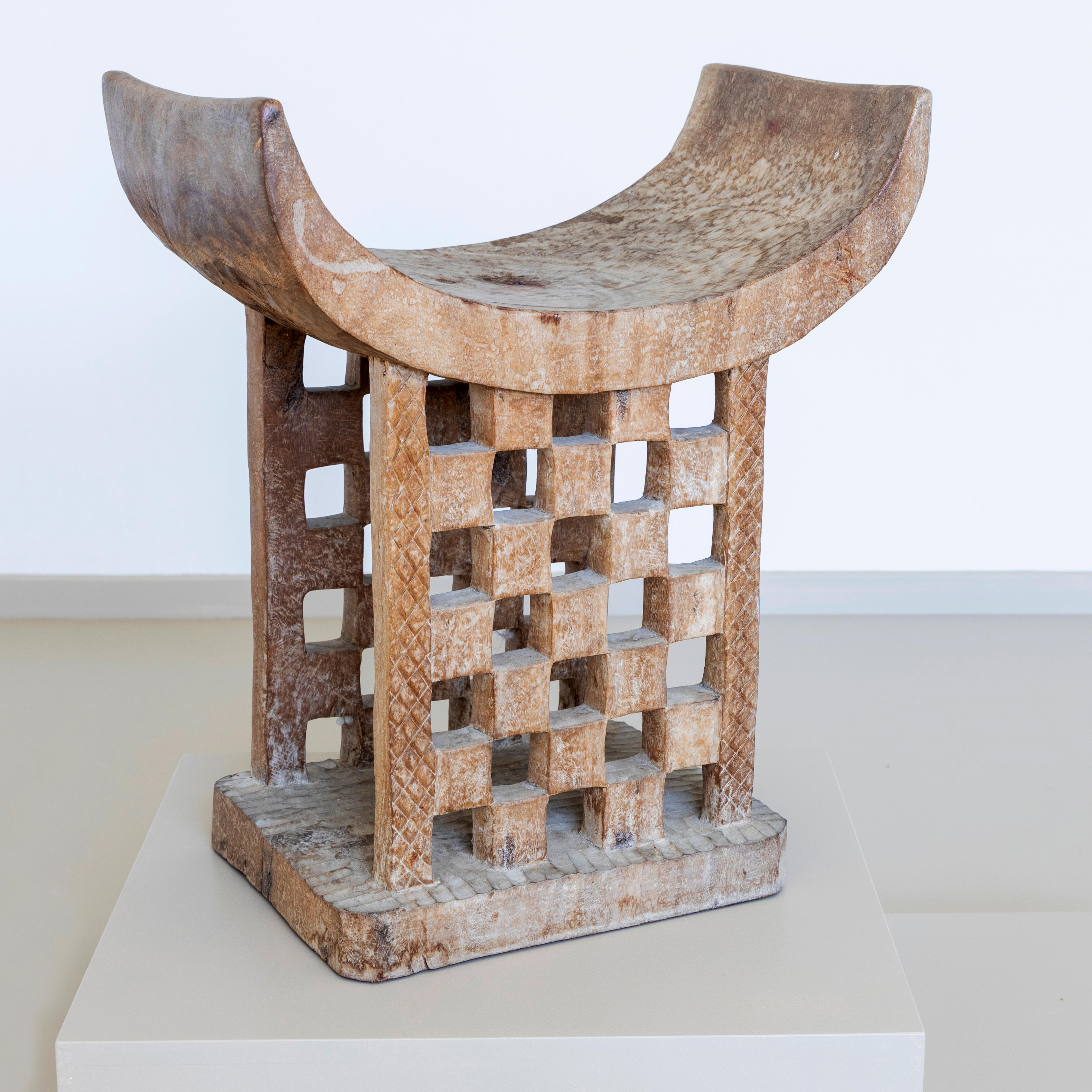 Tabouret africain moderne de style traditionnel. Le tabouret est sculpté dans du bois et blanchi à la chaux. Le tabouret a une assise en forme de bol et une base ajourée avec un motif en damier. 