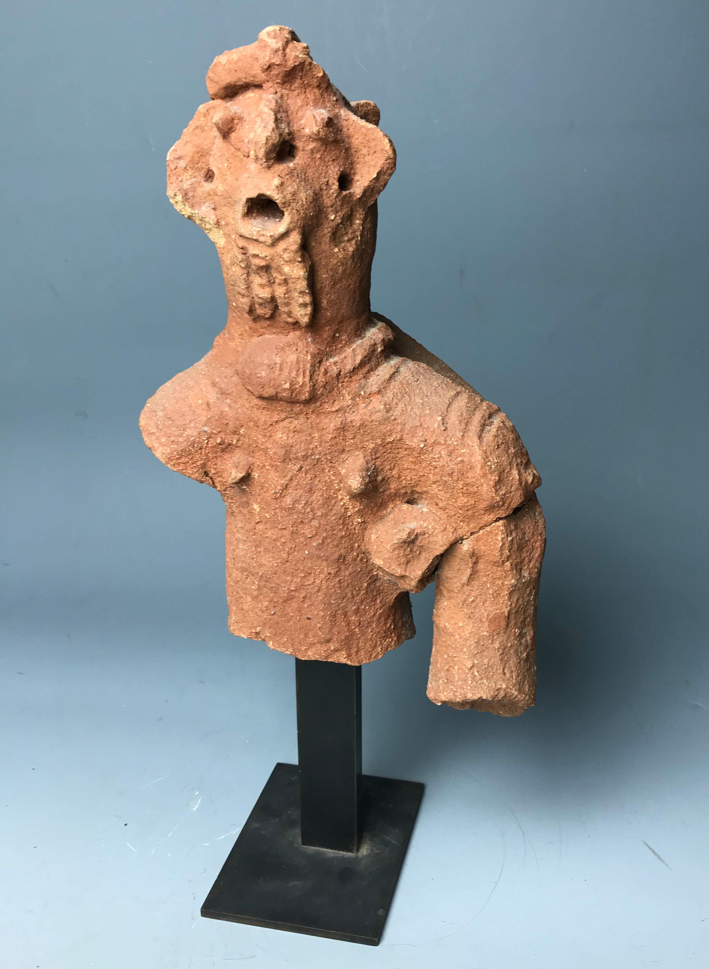 A striking abstract modelled terracotta figural torso the expressive visage gesticulating with open singing mouth and beard and ridged coiffure carrying a object on his back, in heavy solid terracotta with red pigment A splendid and rare example of