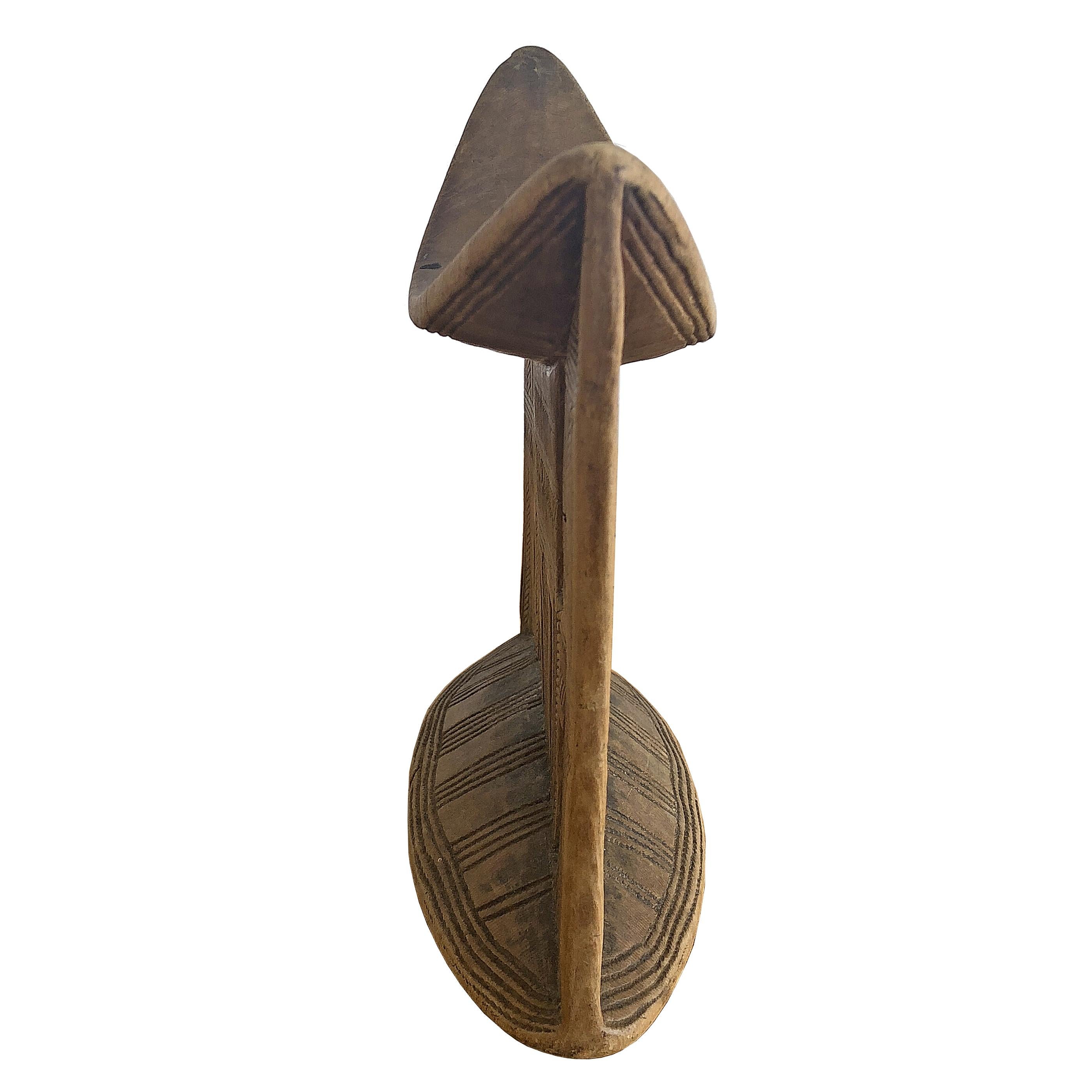 An African tribal headrest in a light, wheat-colored wood with incised geometric carvings from the Sidama People of Ethiopia. Made from a single piece of wood this handsome headrest was made to serve as a utilitarian object to be used in everyday